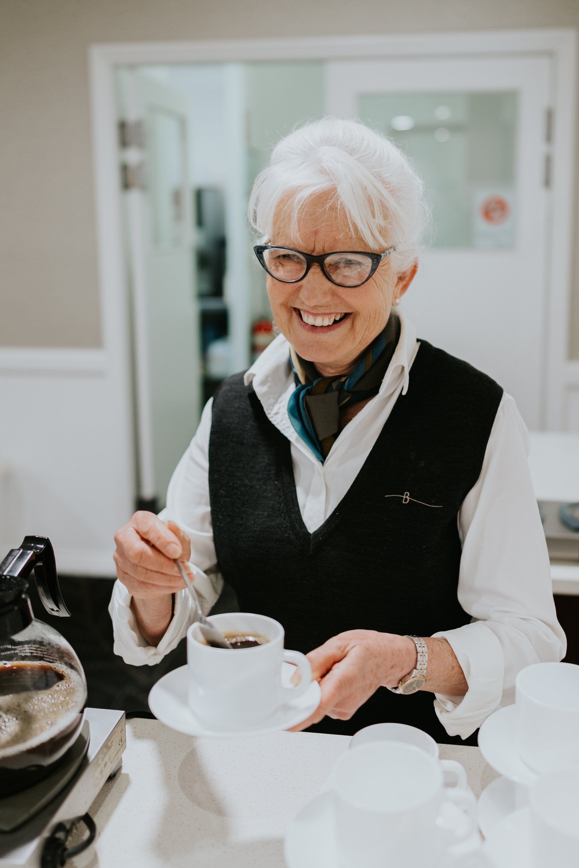 Smiling person pouring tea from a white teapot at a table in a bright cafe