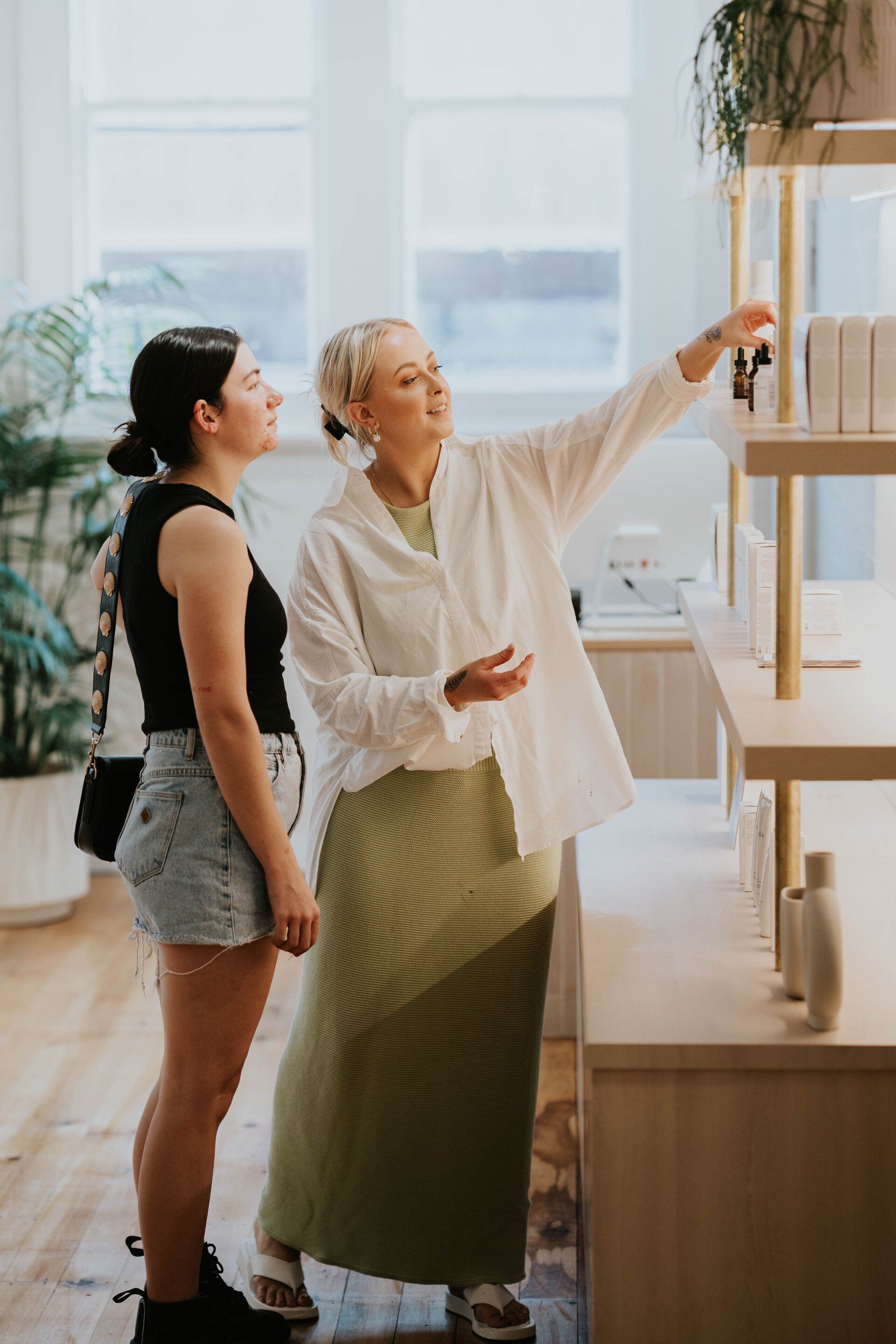 Two women browsing a wooden shelf in a bright, modern home interior