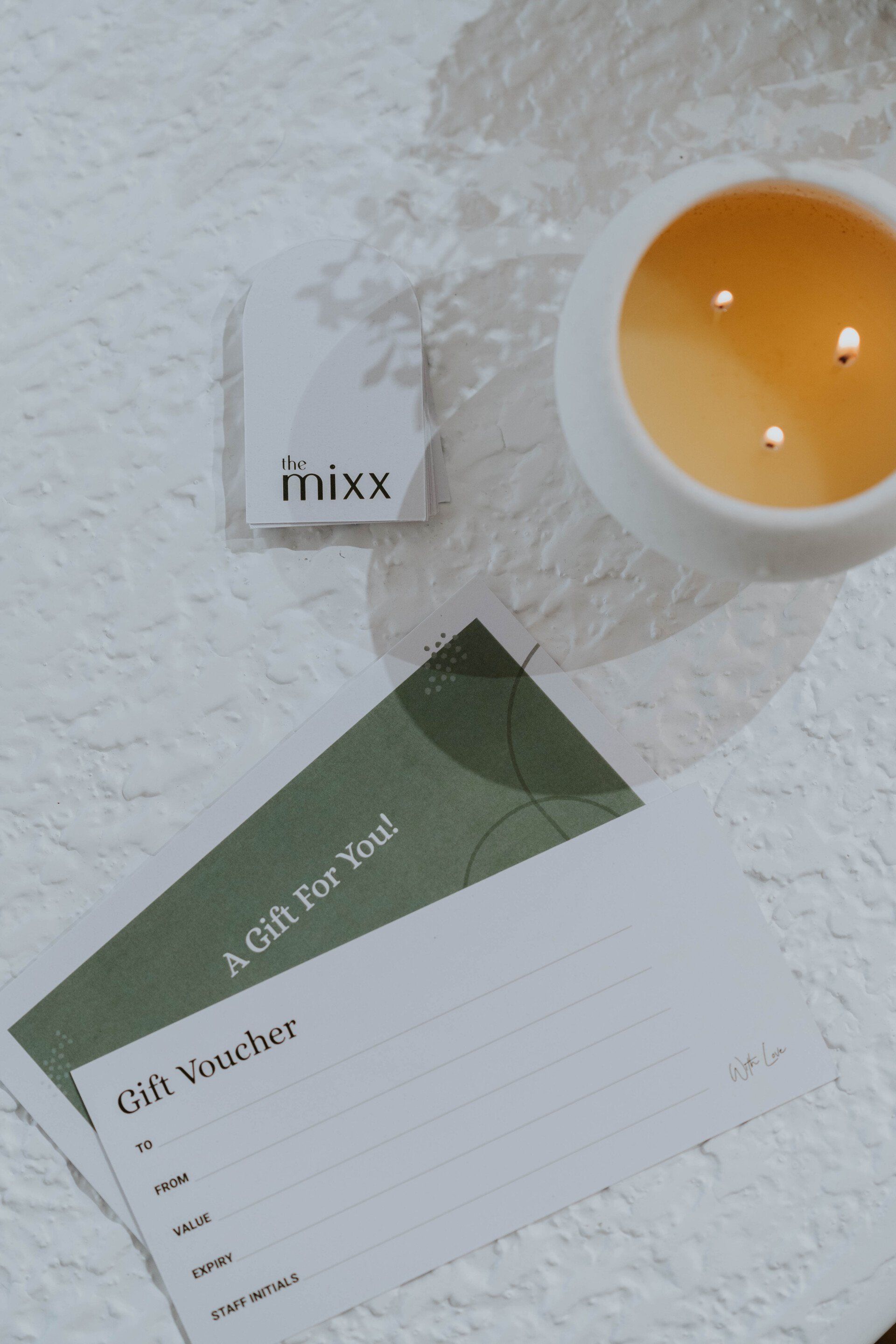 Green-and-white stationery with a small orange candle on a textured white surface.