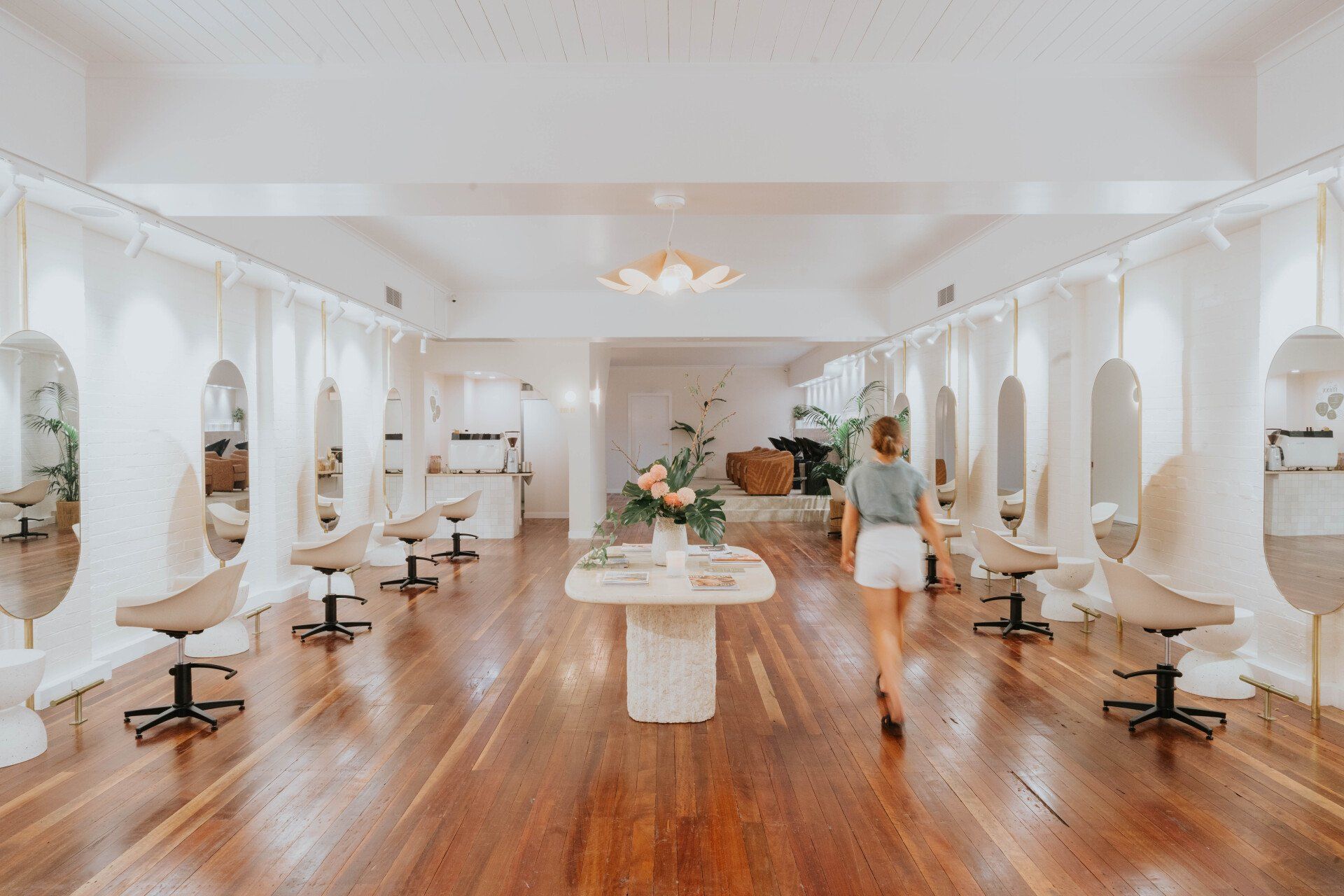 Bright white salon interior with wooden floors, styling chairs, and a person walking down the center aisle