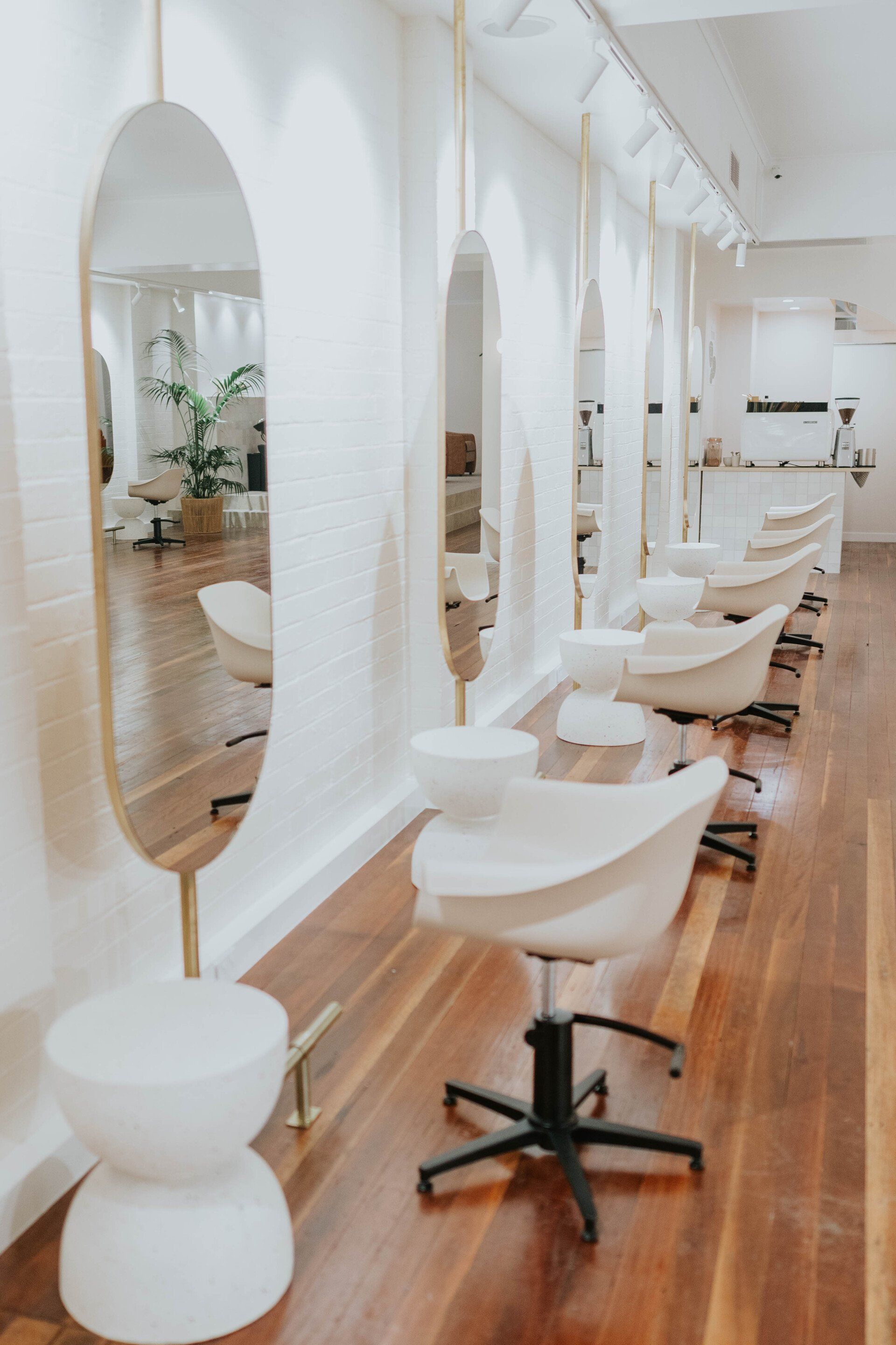 Bright minimalist salon interior with white styling chairs, mirrors, and wooden floors