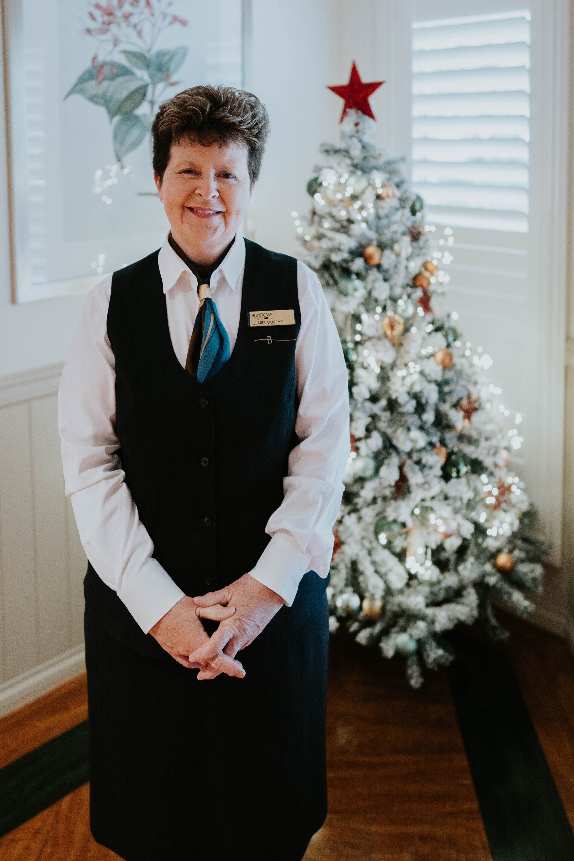 Person standing indoors beside a decorated white Christmas tree with a red star topper.