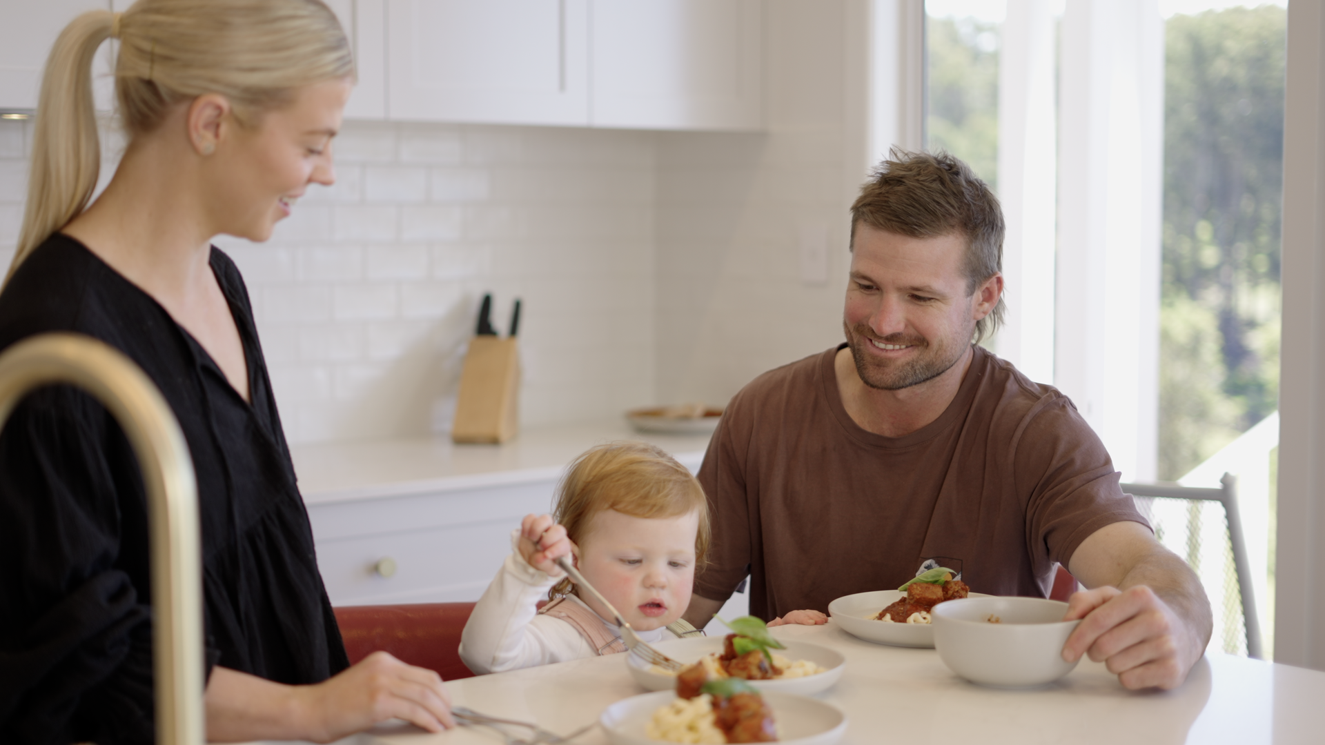 Family eating together at a bright kitchen table, with a woman, child, and man sharing a meal