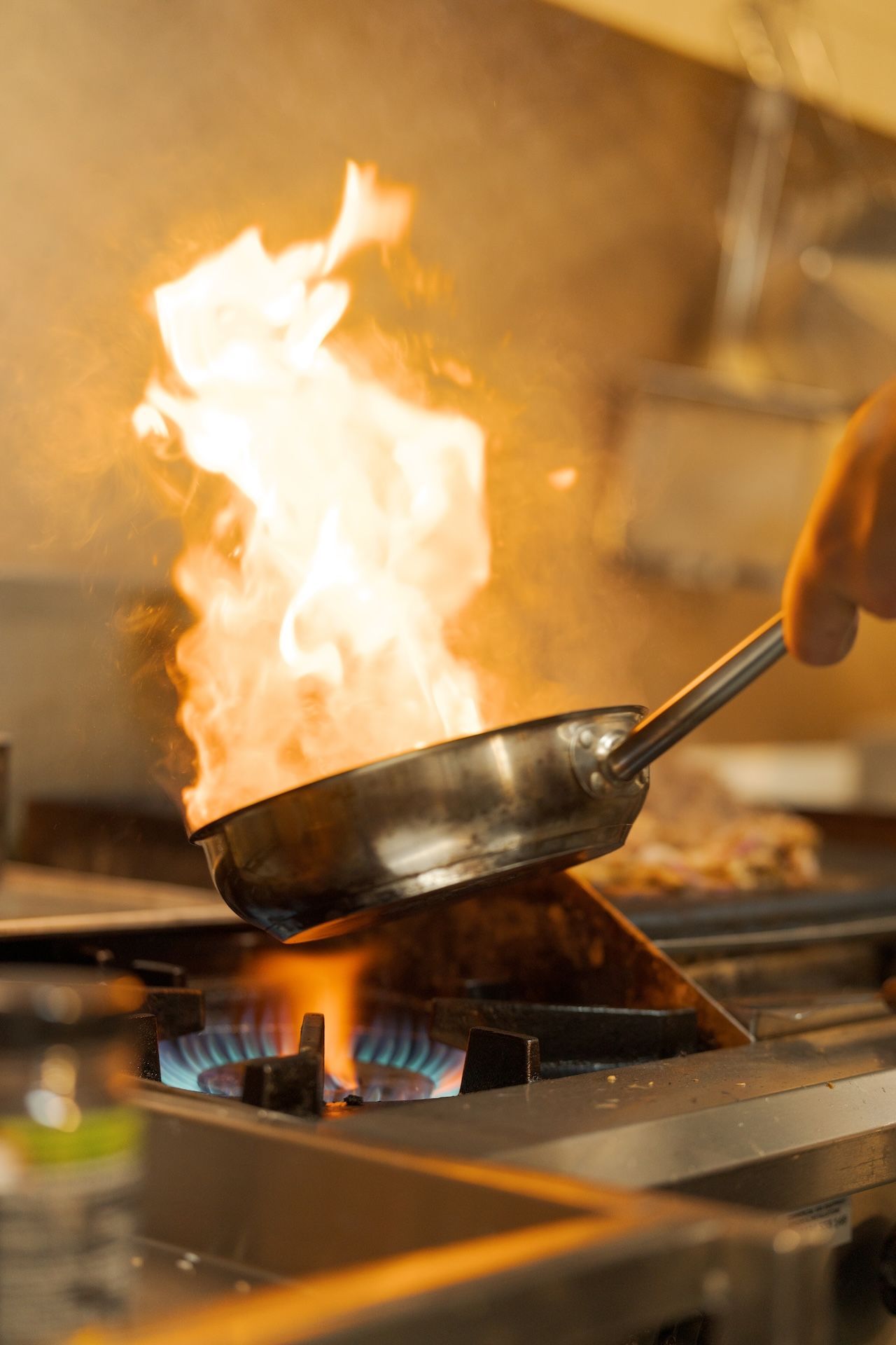Pan of food flaming over a gas stove in a commercial kitchen
