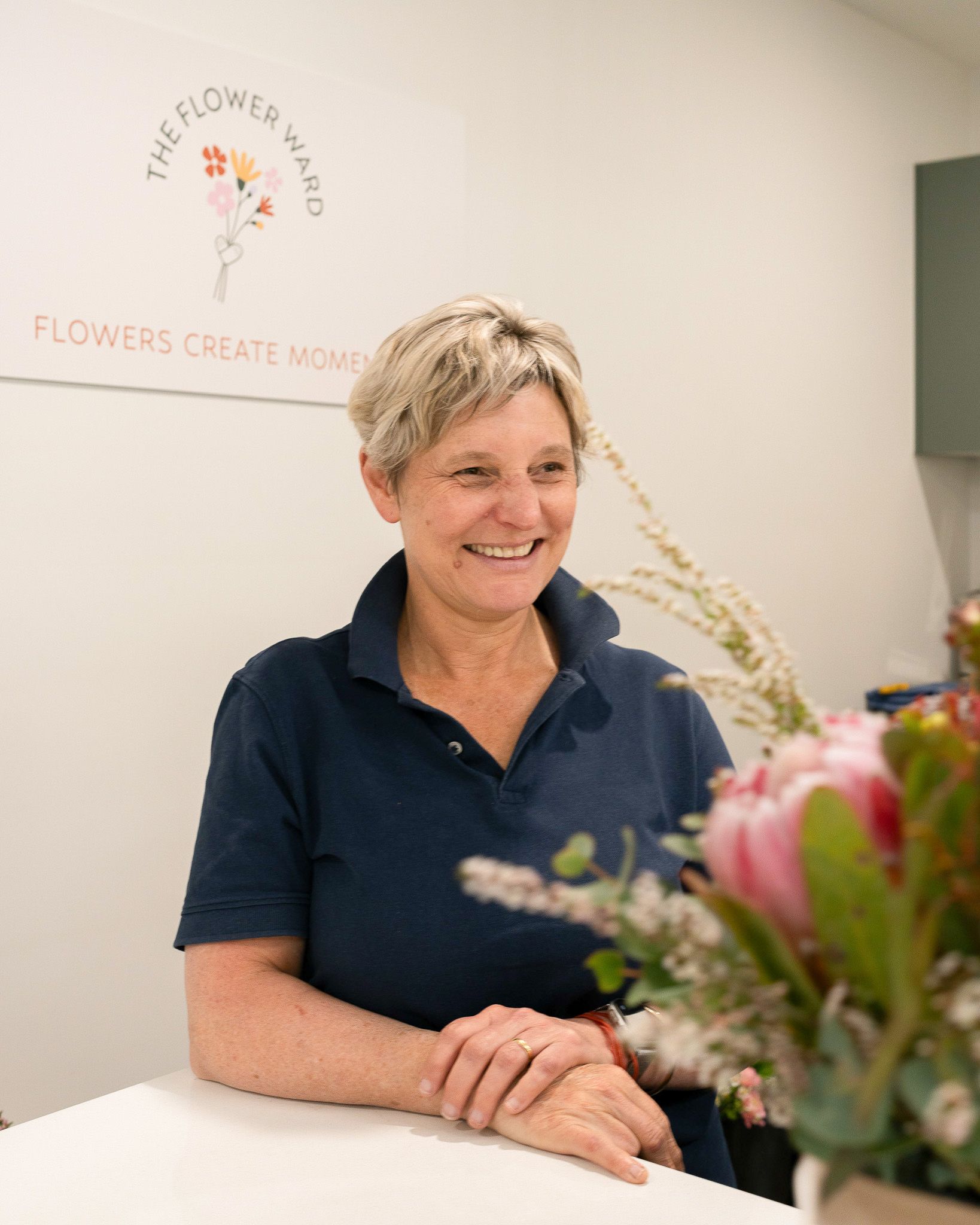 Smiling florist in navy shirt standing behind a counter with colorful flowers in a shop