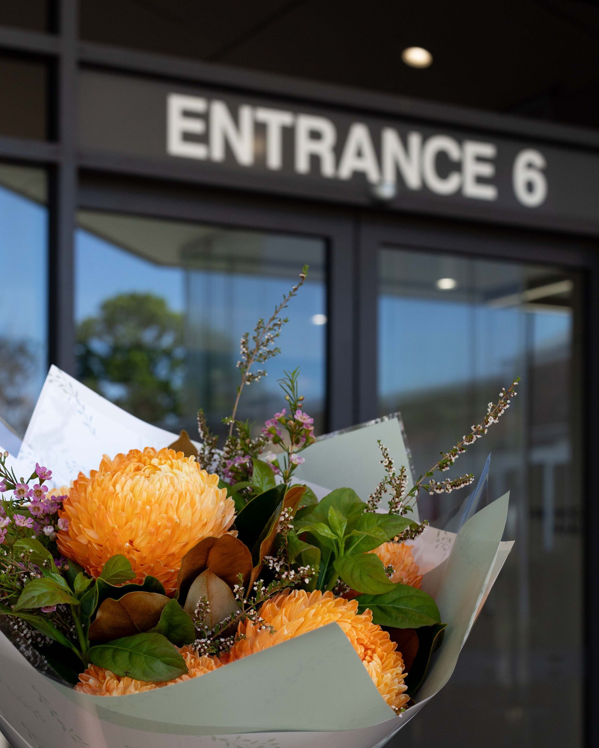 Bouquet of orange flowers held in front of a building entrance labeled “ENTRANCE 6”