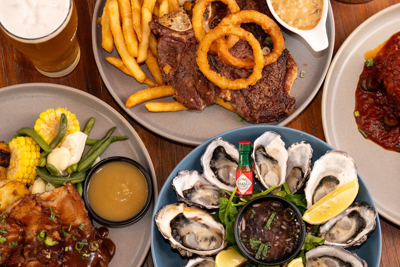 Overhead view of assorted pub foods: oysters, fries, onion rings, steak, and a beer on a wooden table