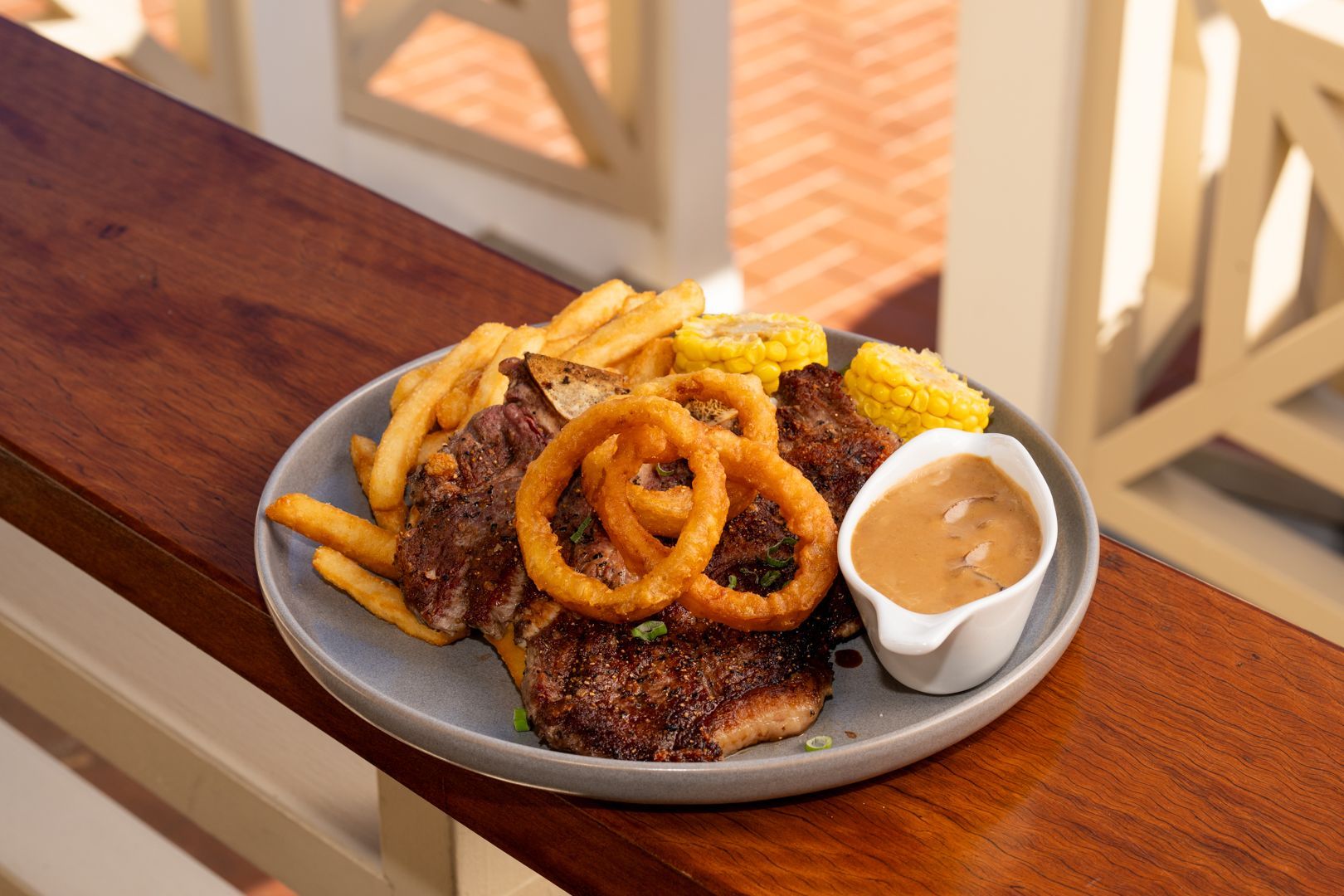 Plate of fried food with onion rings and dipping sauce on a wooden railing, with a drink in the background