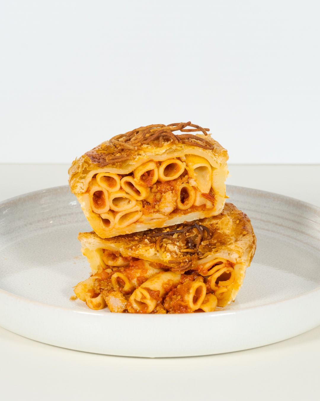 Two stacked slices of baked pasta with golden cheese on a white plate