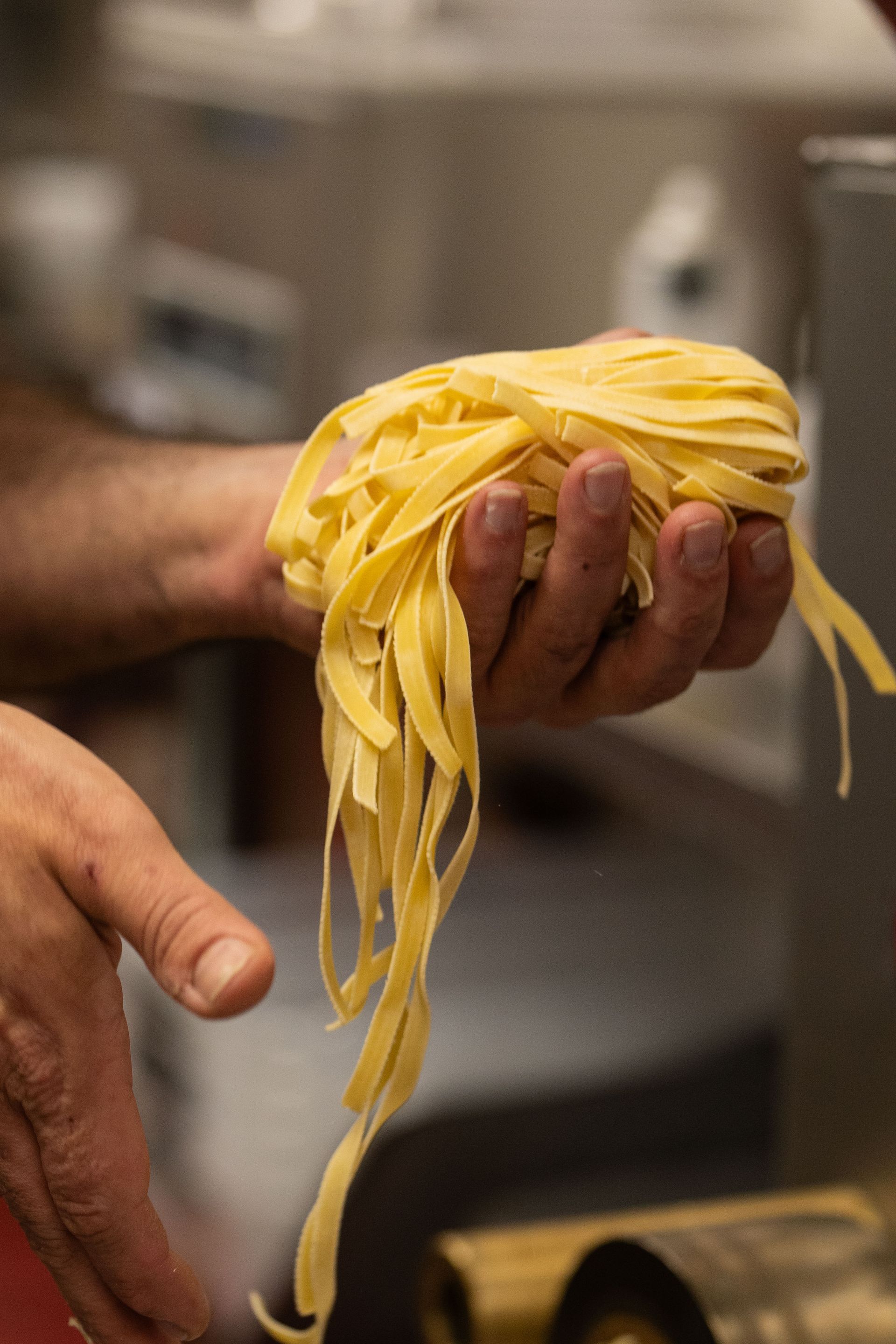 Hand holding a bundle of yellow pasta strands in a kitchen
