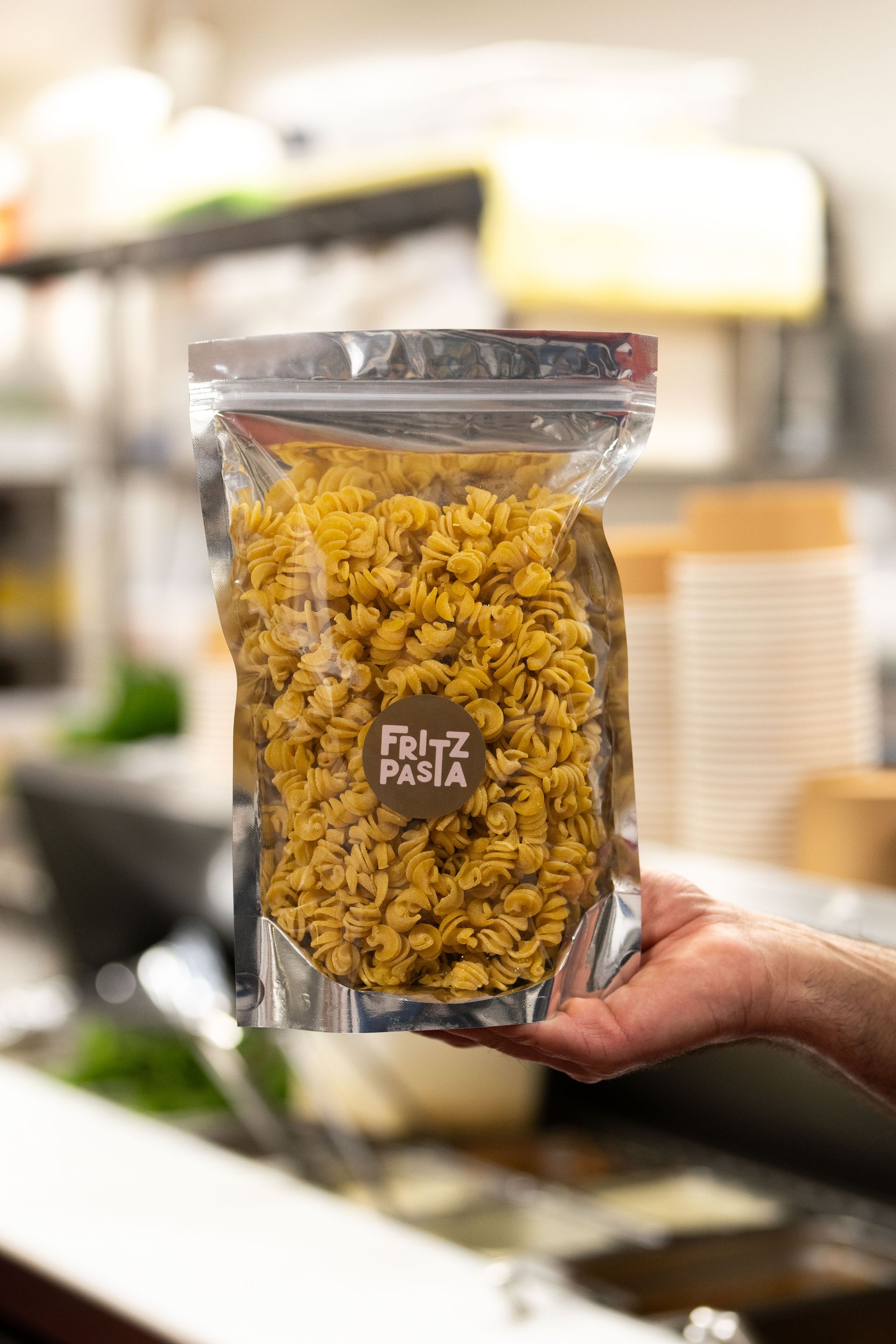 Hand holding a clear pouch of yellow pasta in a grocery store aisle