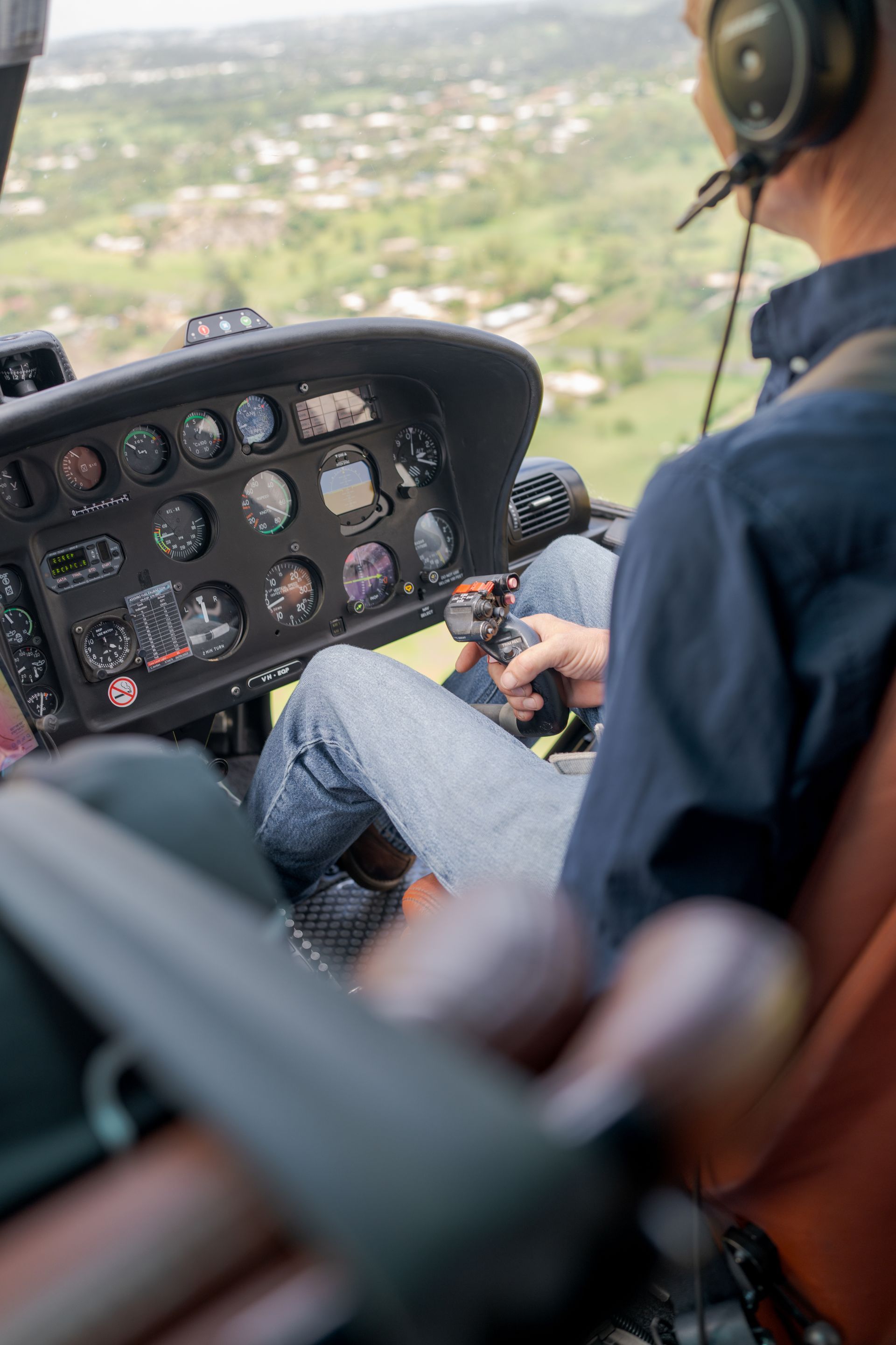 Helicopter cockpit view with pilot flying over a green landscape