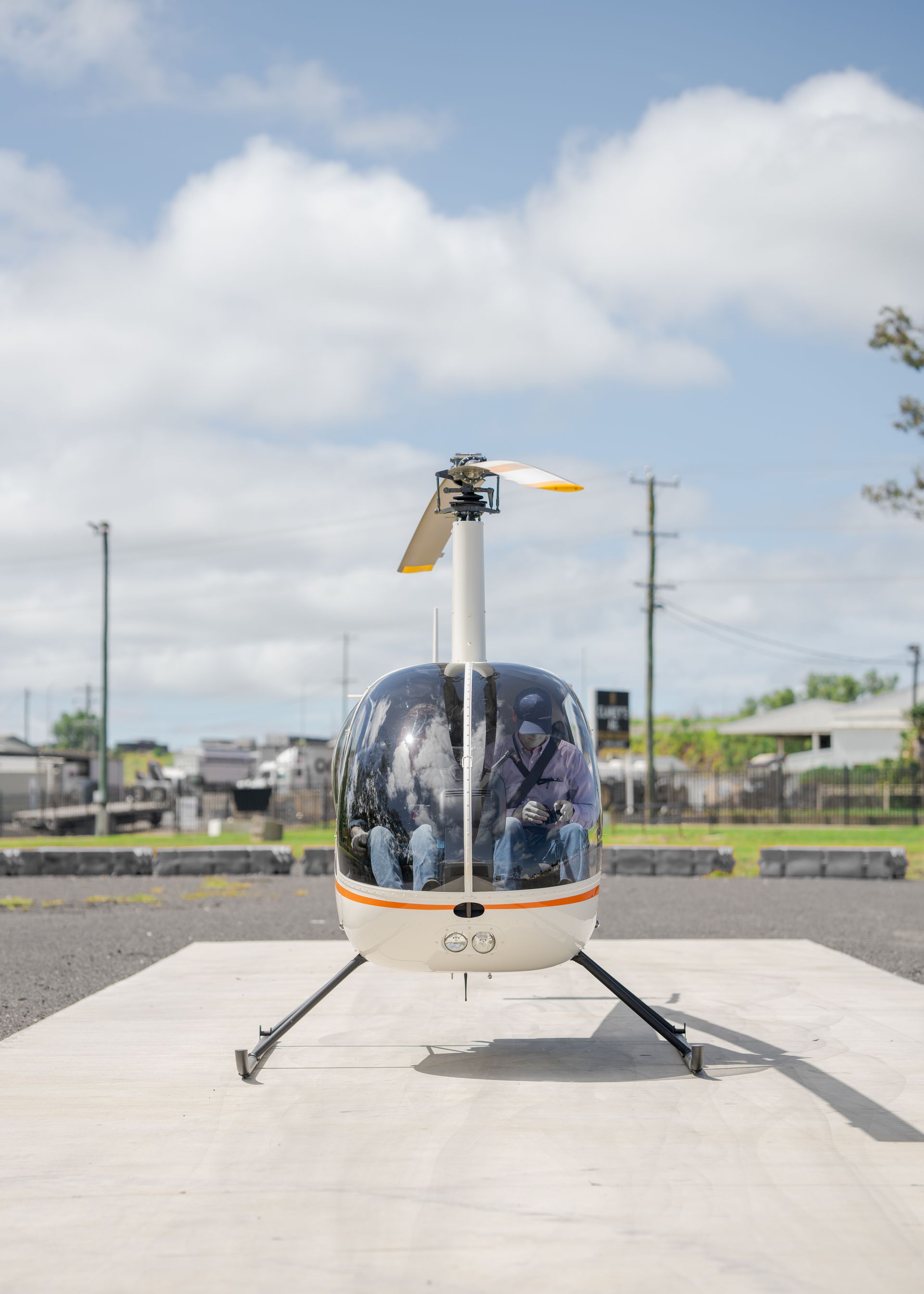 Small white helicopter parked on a concrete pad under a cloudy sky