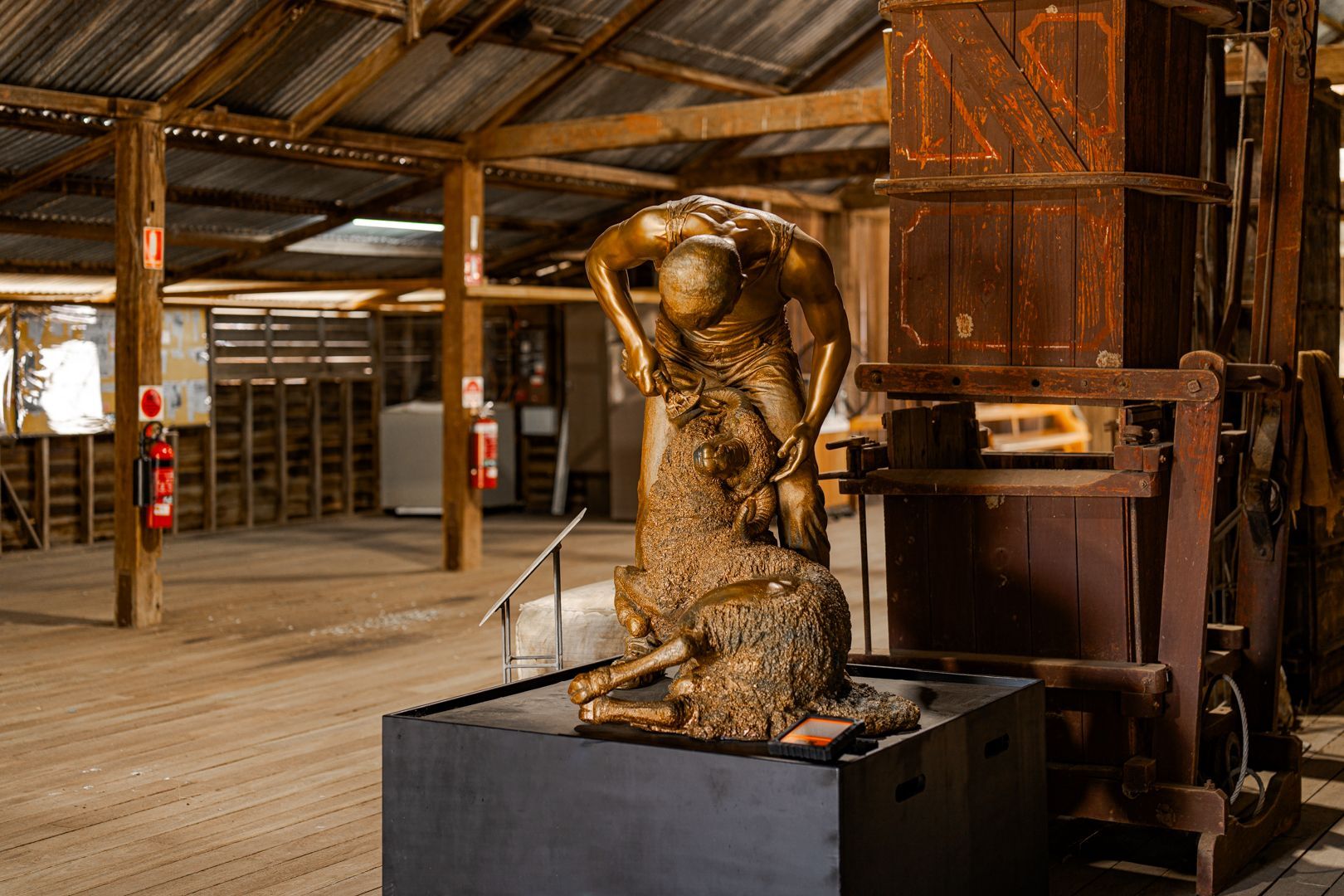 Bronze sculpture of a bending human figure in a rustic wooden museum or workshop interior