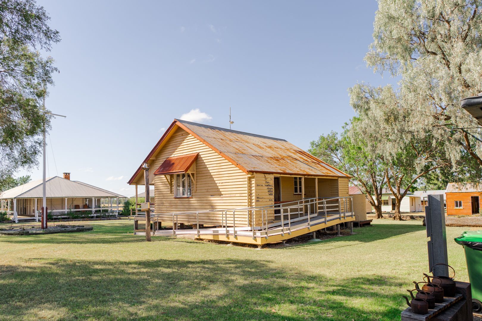 Wooden cabin with porch in a grassy park, trees and blue sky around it.