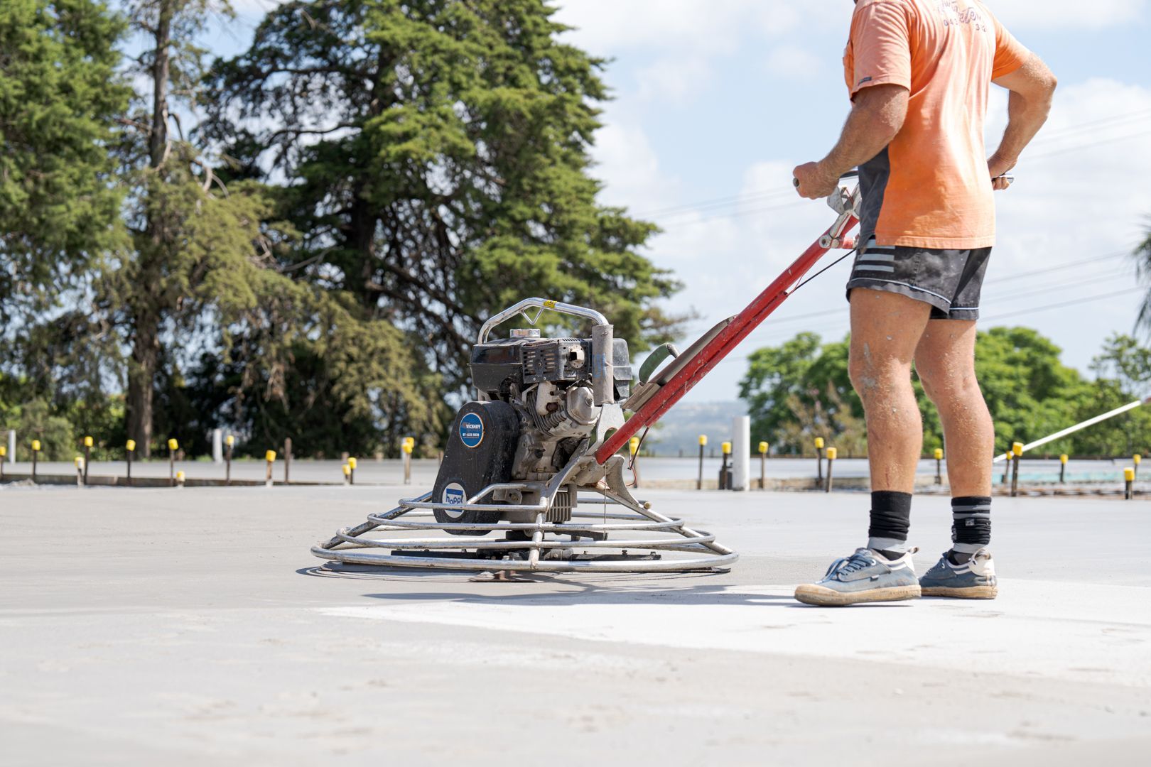 Person operating a power trowel on a concrete surface outdoors.