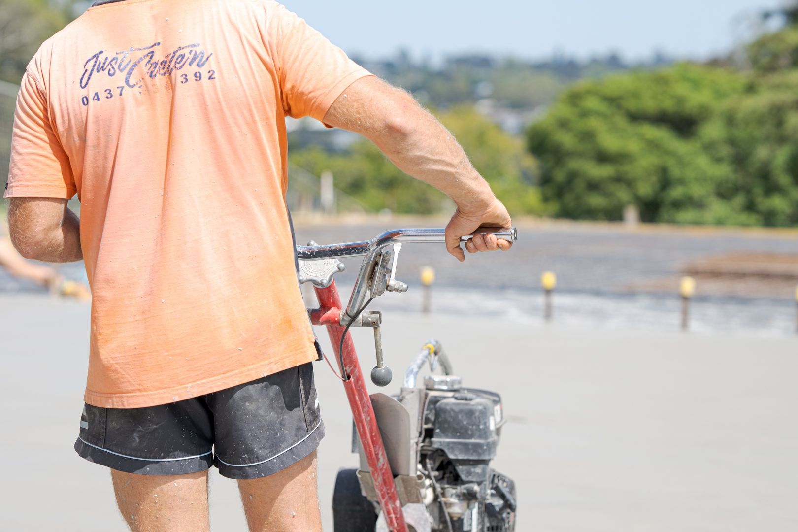Person in a peach shirt standing beside a bicycle on a sunny waterfront path