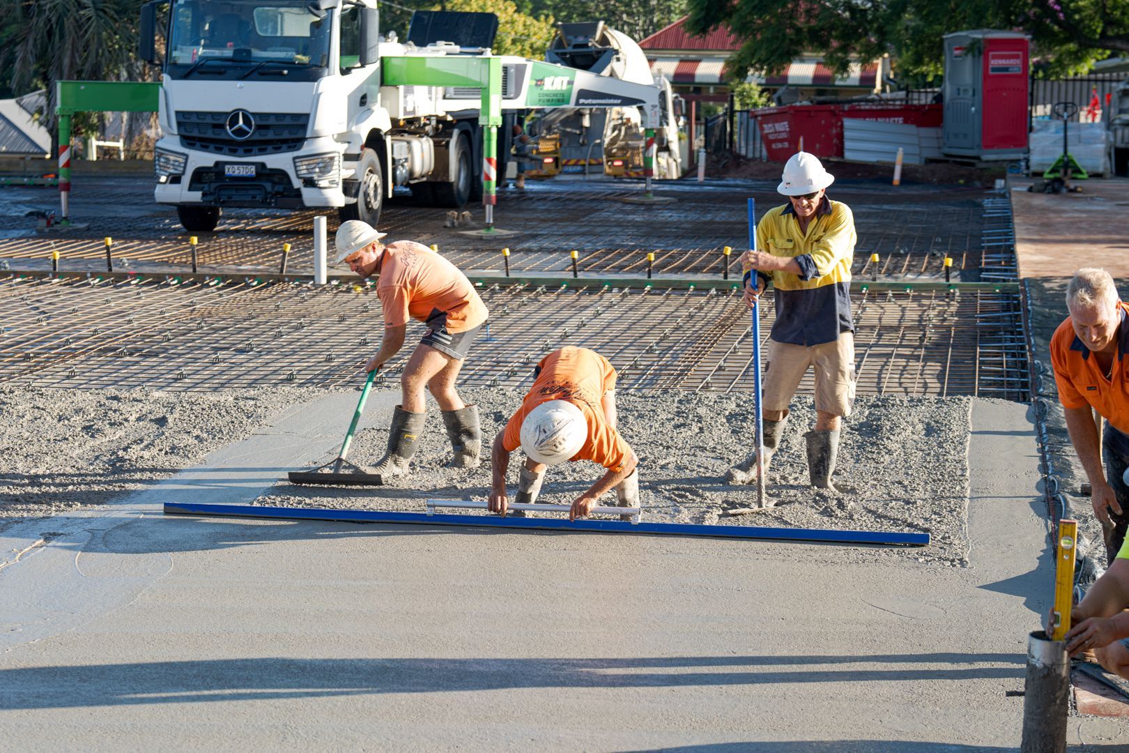 Construction workers spreading wet concrete on a road with tools and a truck in the background