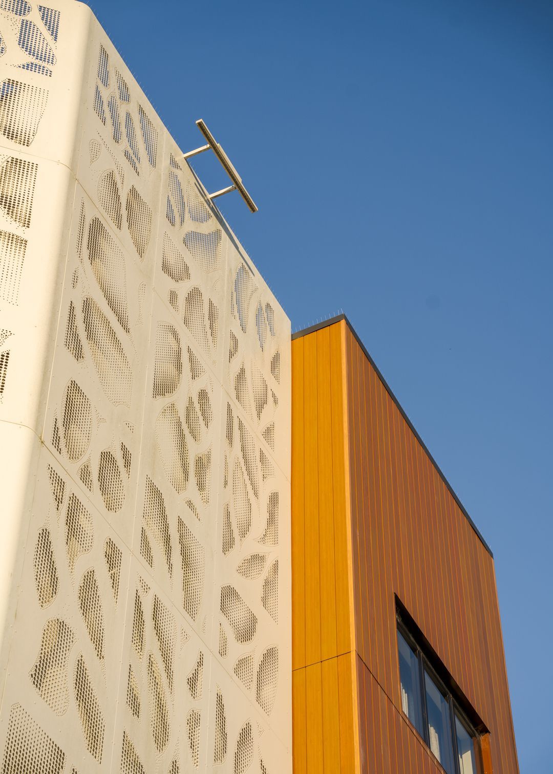 Modern building facade with white patterned wall and orange panel against a blue sky