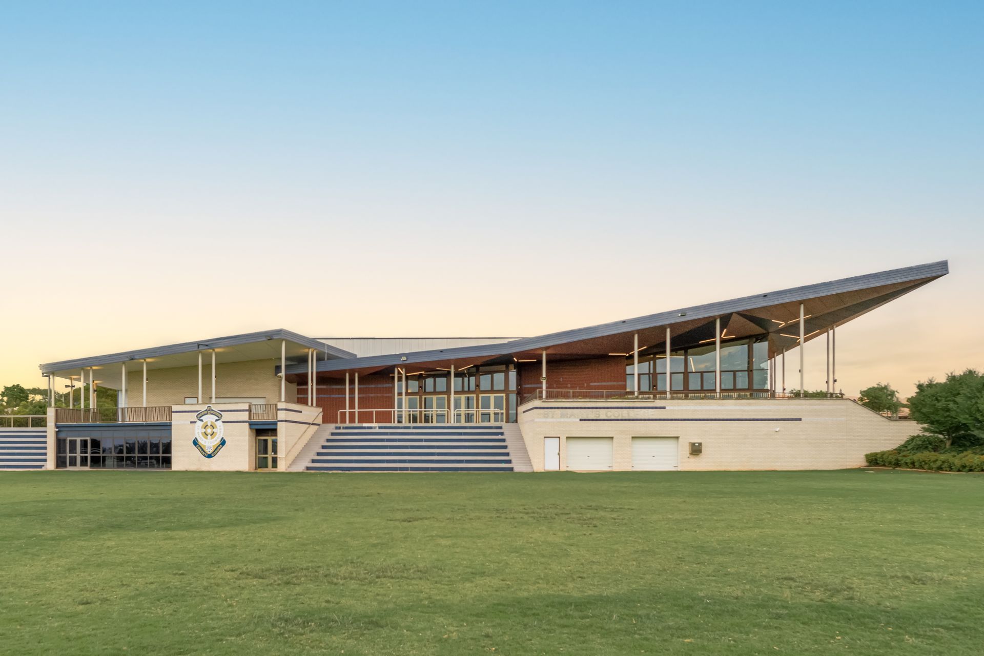 Modern low building with a slanted roof on a grassy field at sunset