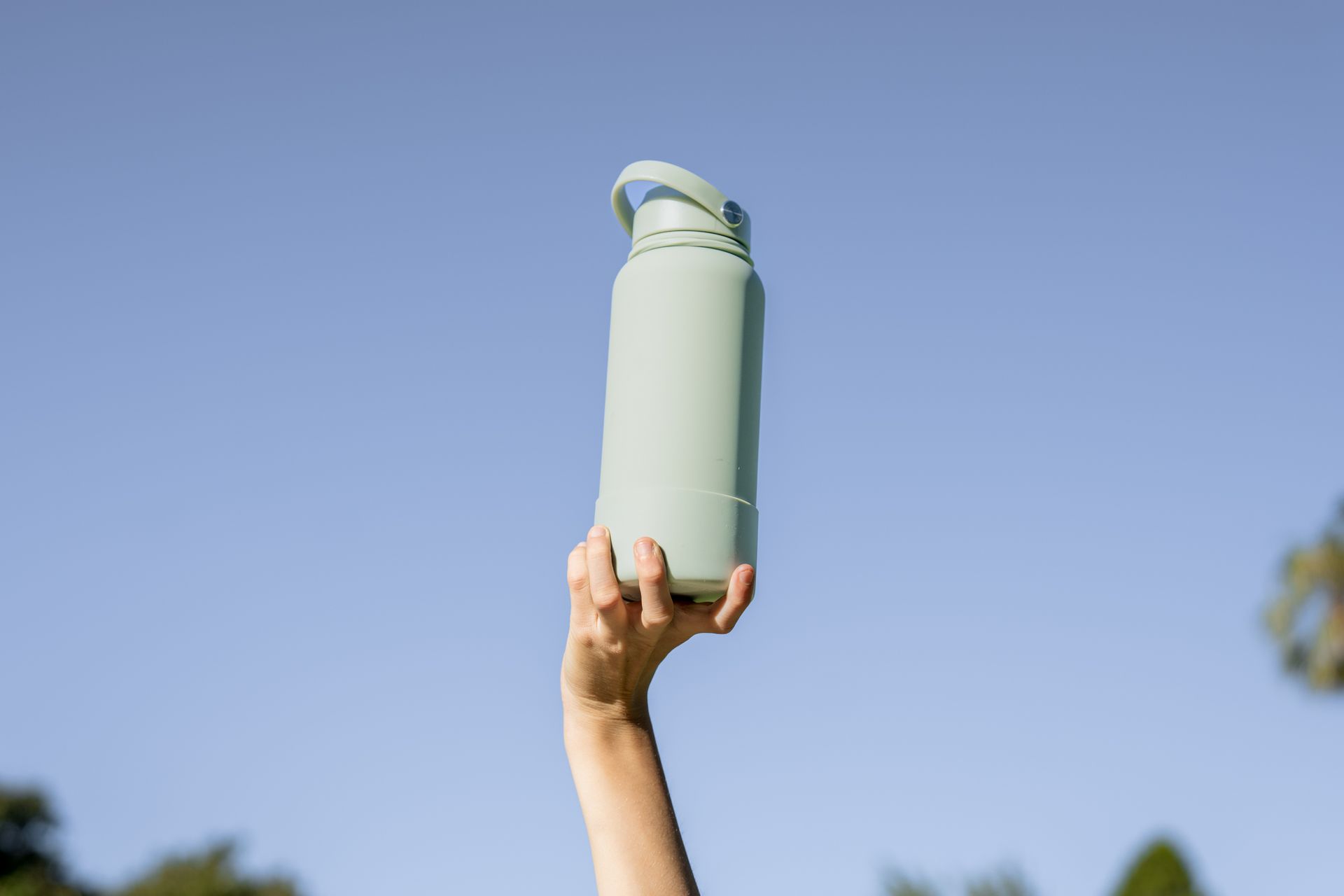 Hand holding a light blue water bottle against a clear blue sky