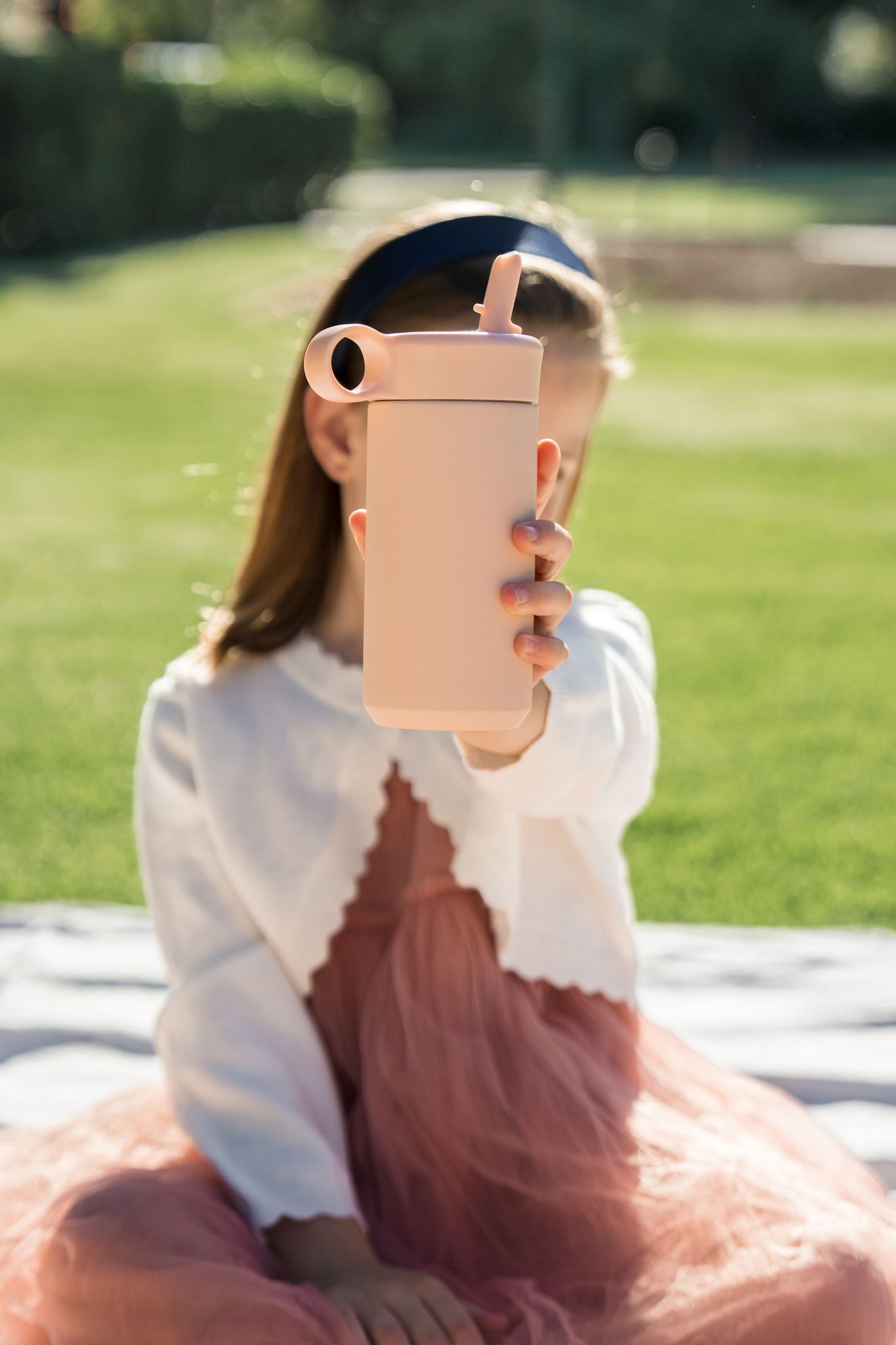 Child seated on a blanket outdoors, holding a phone in a sunny park.
