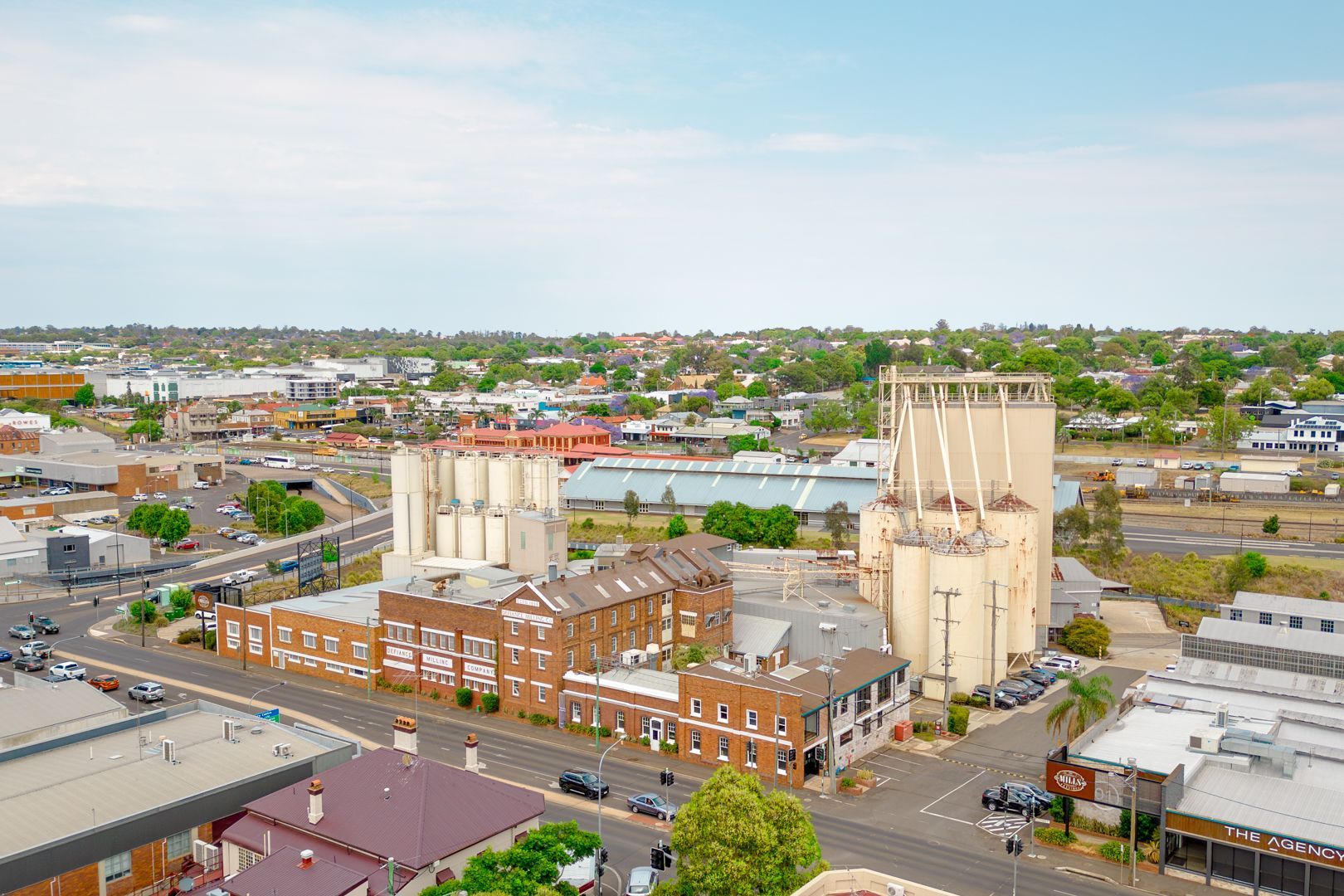 Aerial view of an industrial building complex with silos and surrounding city streets under a clear sky