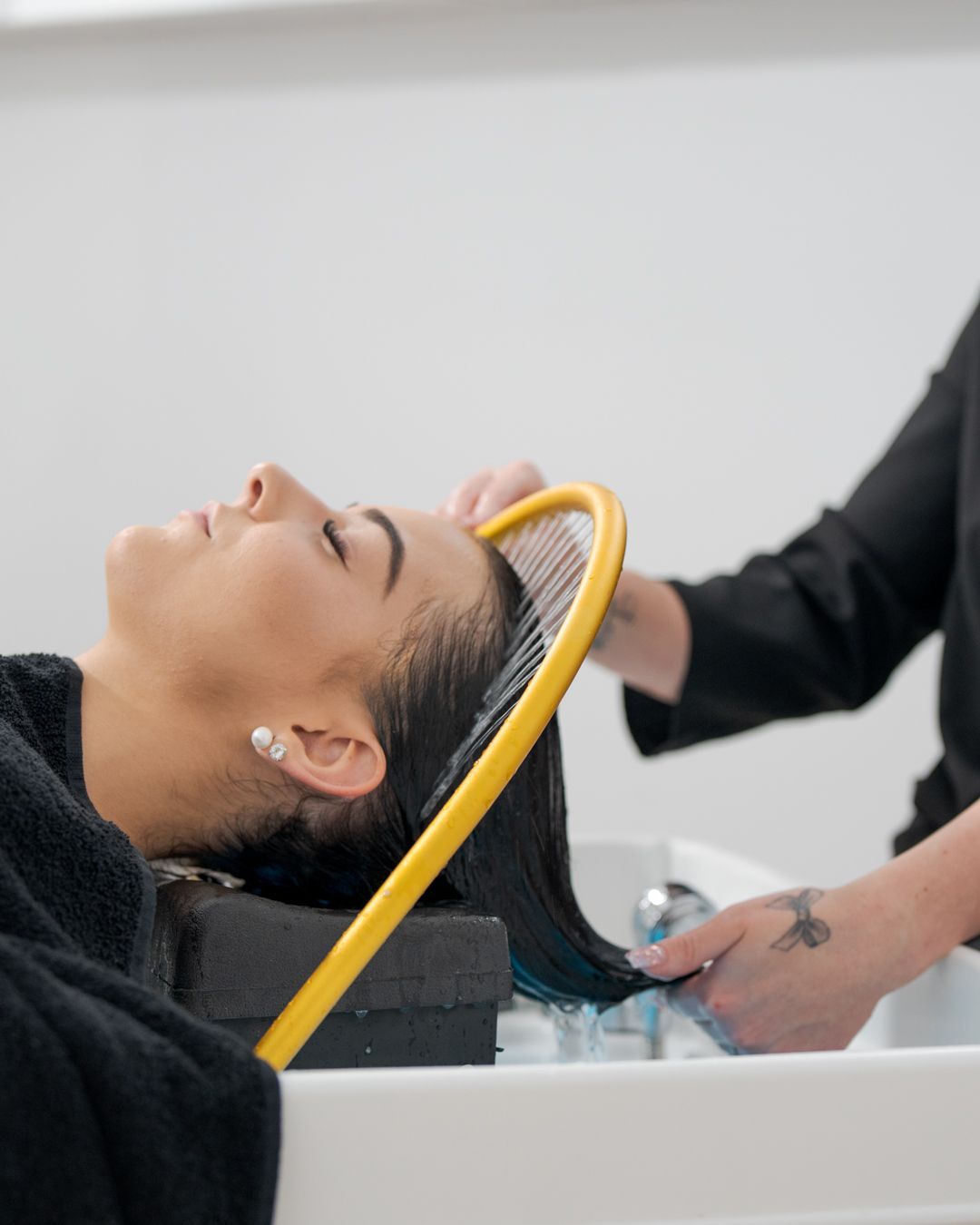 Woman reclining at a salon sink while hair is being rinsed with a yellow hose