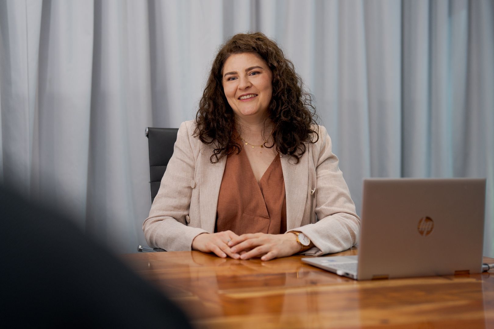 Woman seated at a wooden desk with a laptop, smiling in an office setting