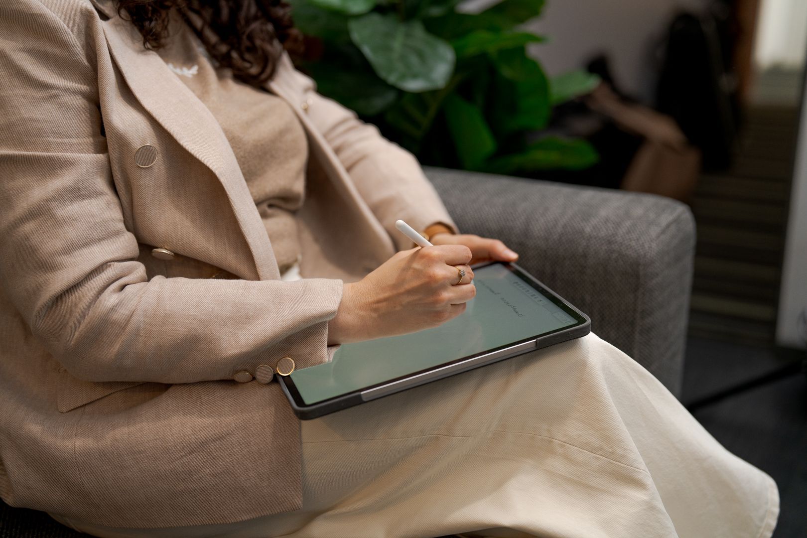 Person using a stylus on a tablet while seated on a gray couch