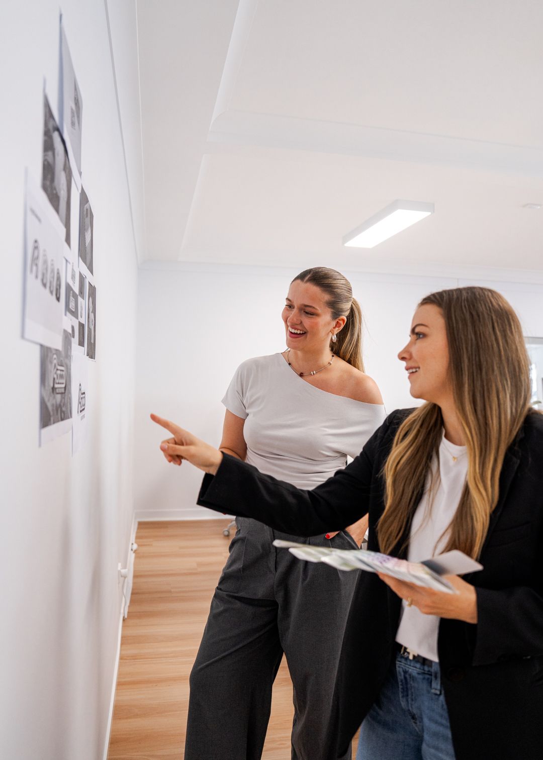 Two coworkers reviewing documents on a wall in a bright office hallway