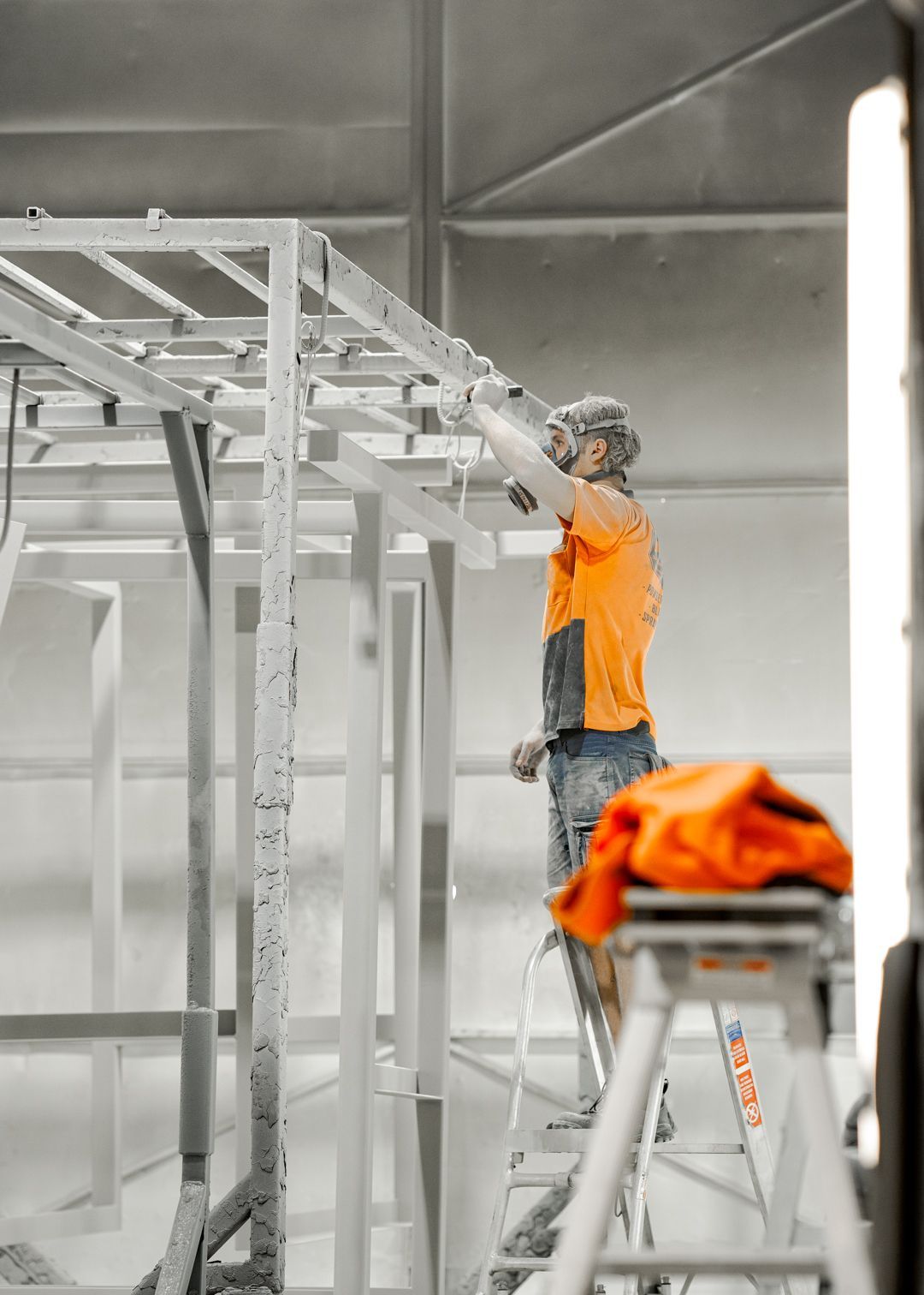 Worker in orange vest painting a metal structure in an industrial workshop