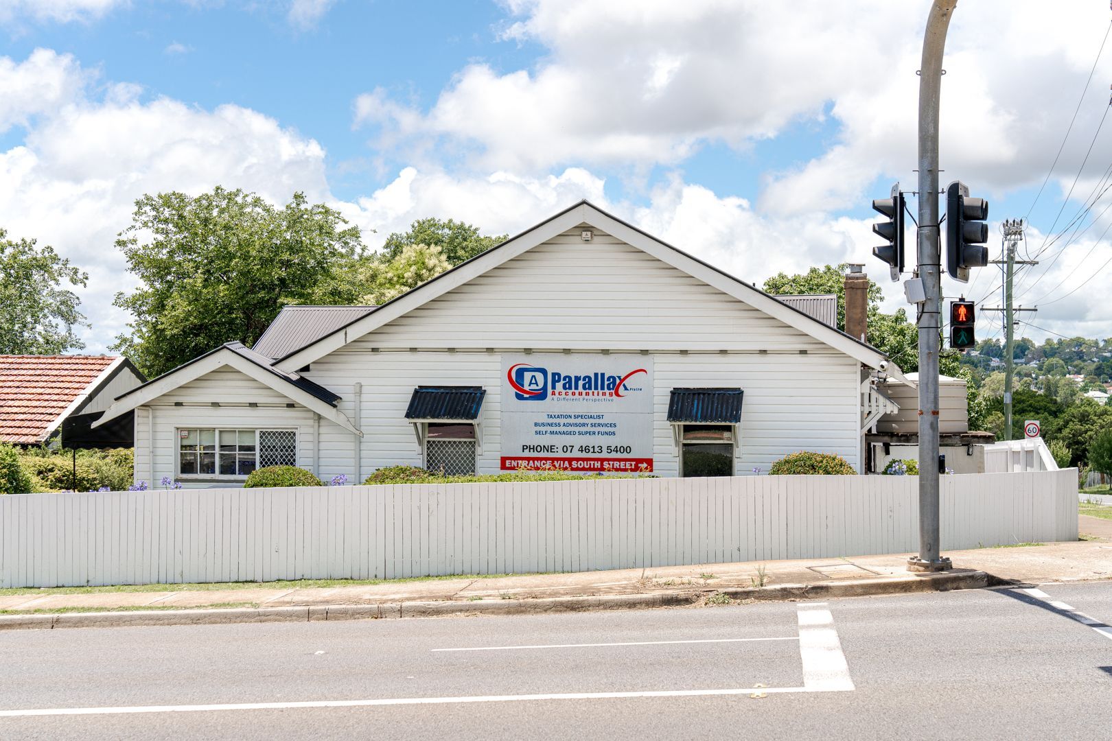 White house behind a fence at a street corner, with a business sign and traffic lights nearby