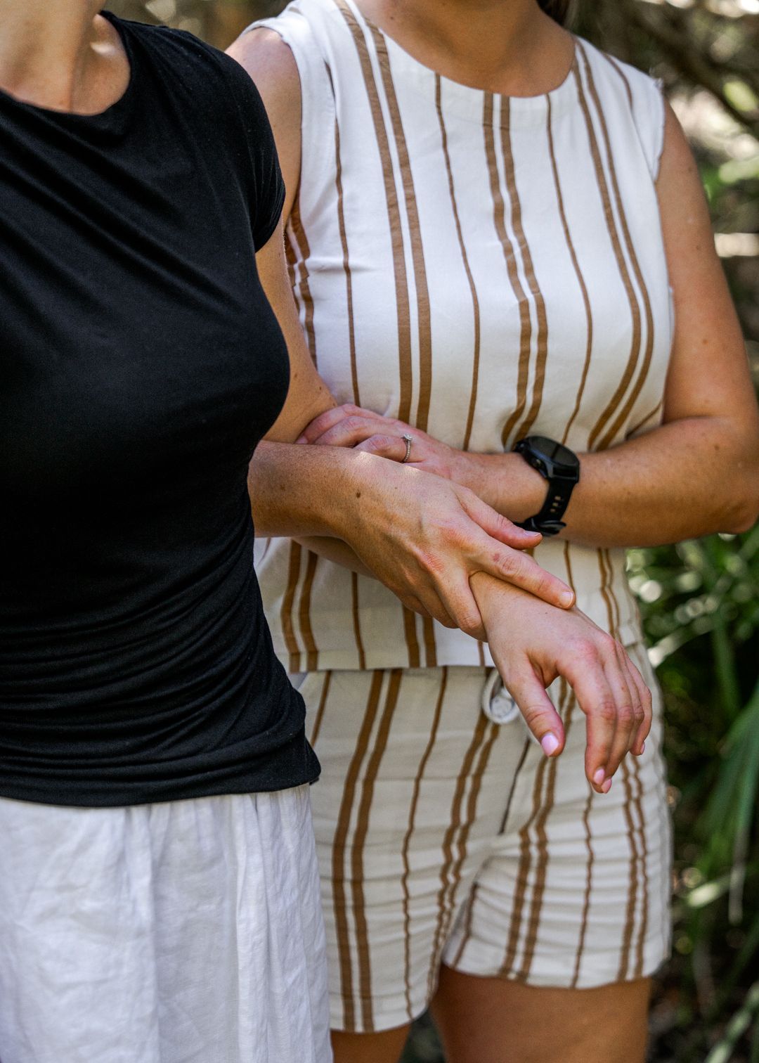 Two people standing close together, one holding the other’s wrist, outdoors.