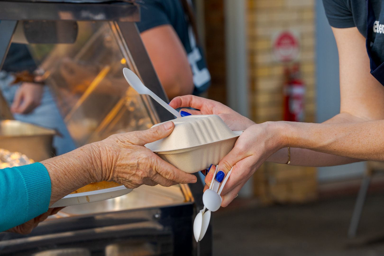 Hands passing a takeout container at a food truck window