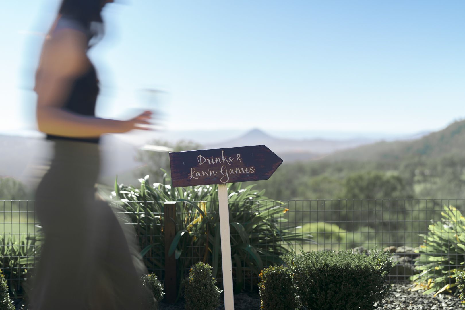 Blurred woman walking past a wedding welcome sign in a sunny garden with hills in the background