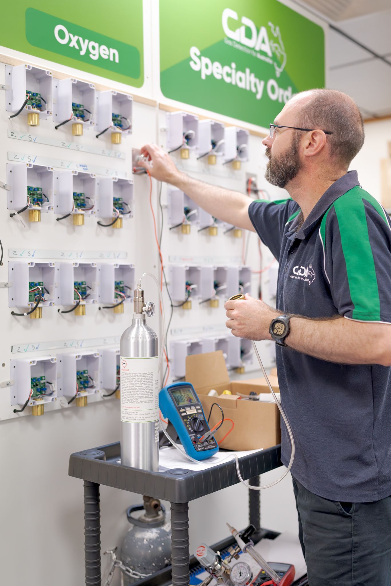 Man in a green shirt reaching for product bottles on a pharmacy wall display labeled Oxygen and Specialty Orders