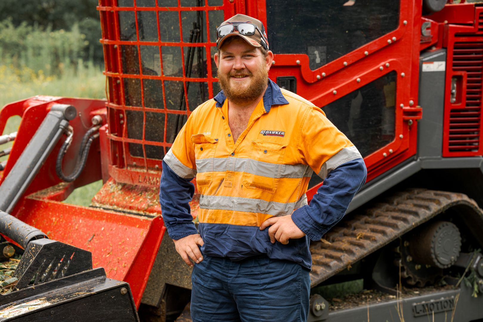 Worker in orange safety gear standing beside a red construction machine outdoors
