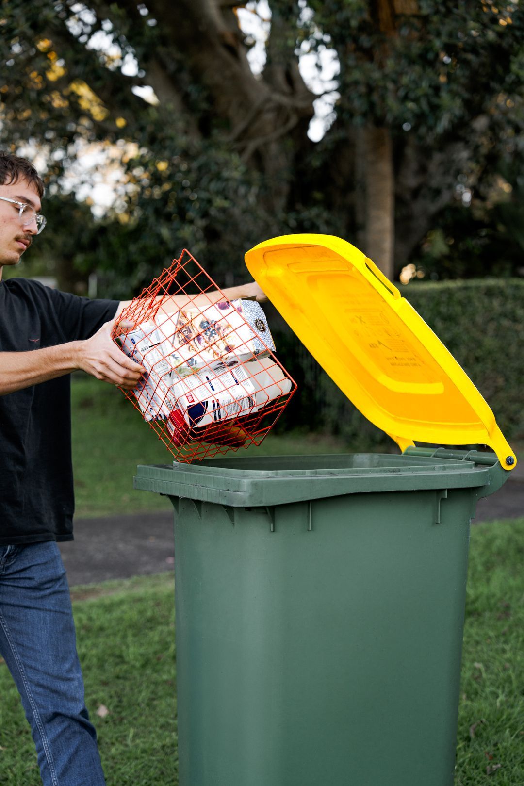 Person tipping a bag of trash into a green curbside bin with a yellow lid