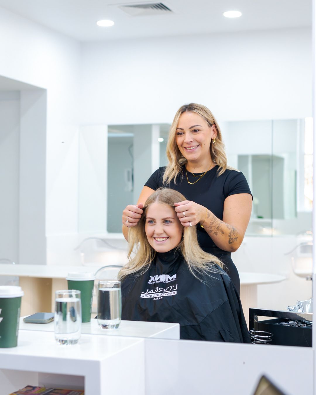 Hairdresser styling a smiling client in a bright salon, with a mirror and white counters in view
