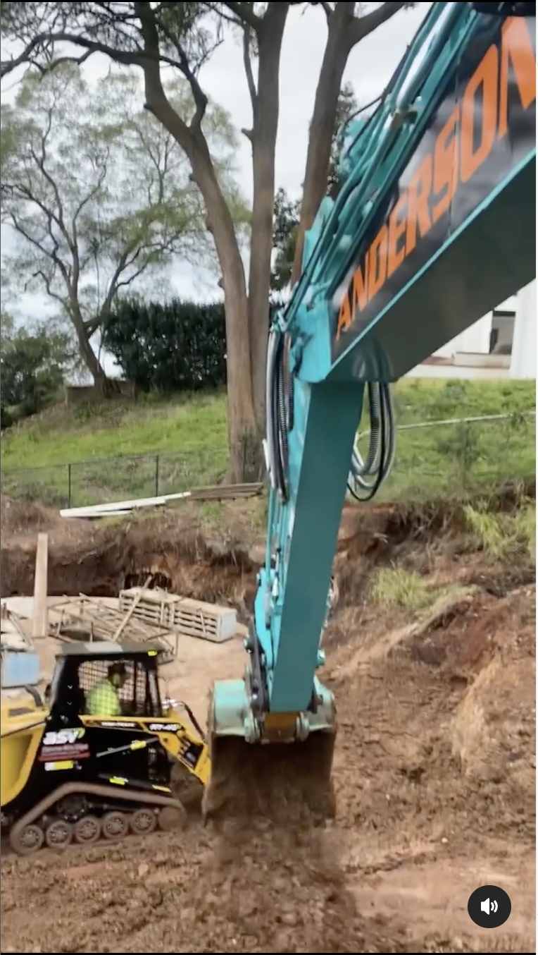 Turquoise excavator digging earth beside a yellow skid steer at a muddy construction site