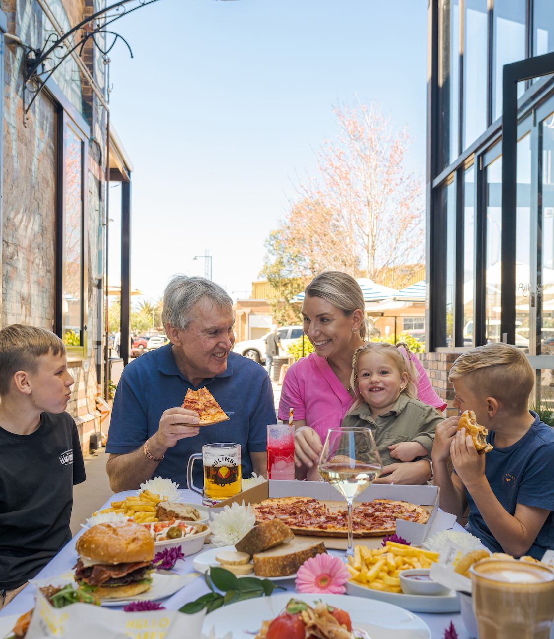 Family sharing pizza and drinks at an outdoor restaurant table in bright daylight