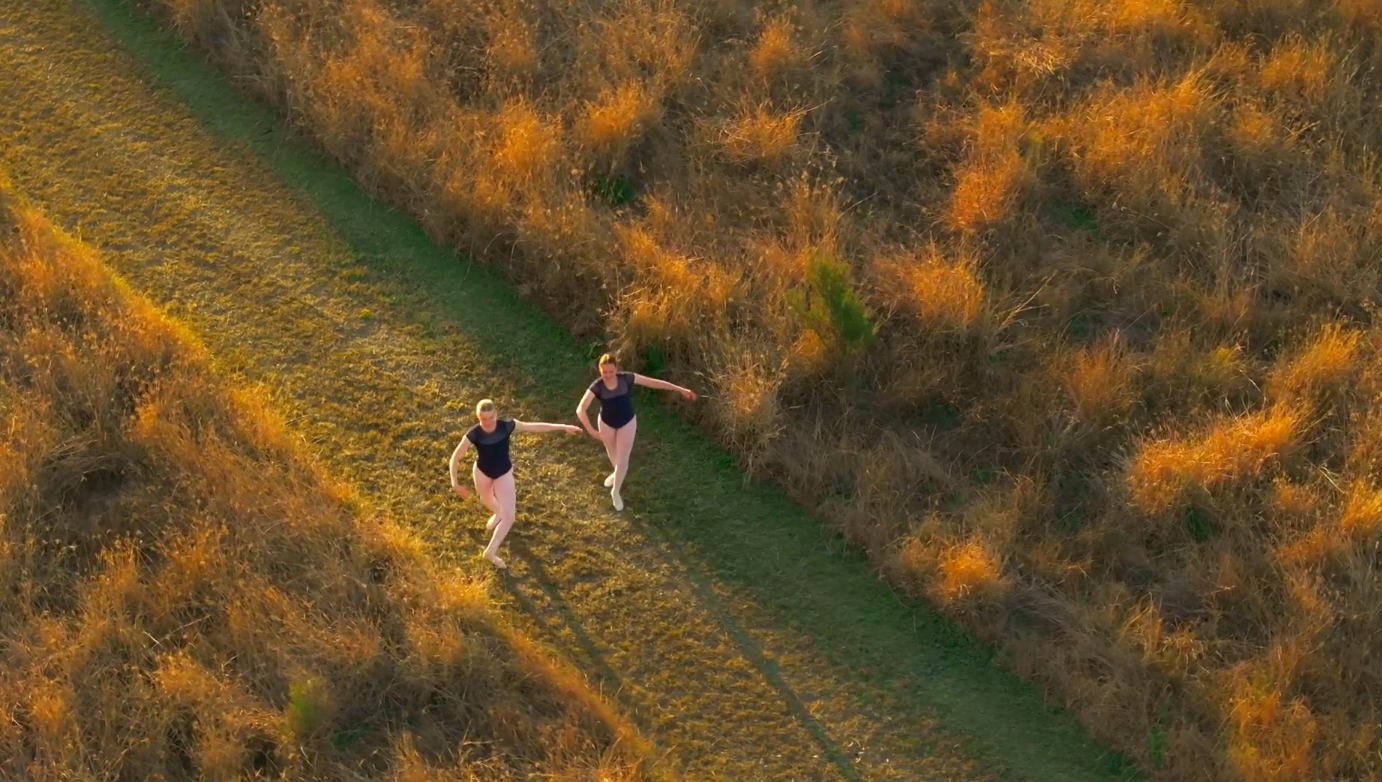 Two hikers walking along a narrow path through golden grassland at sunset