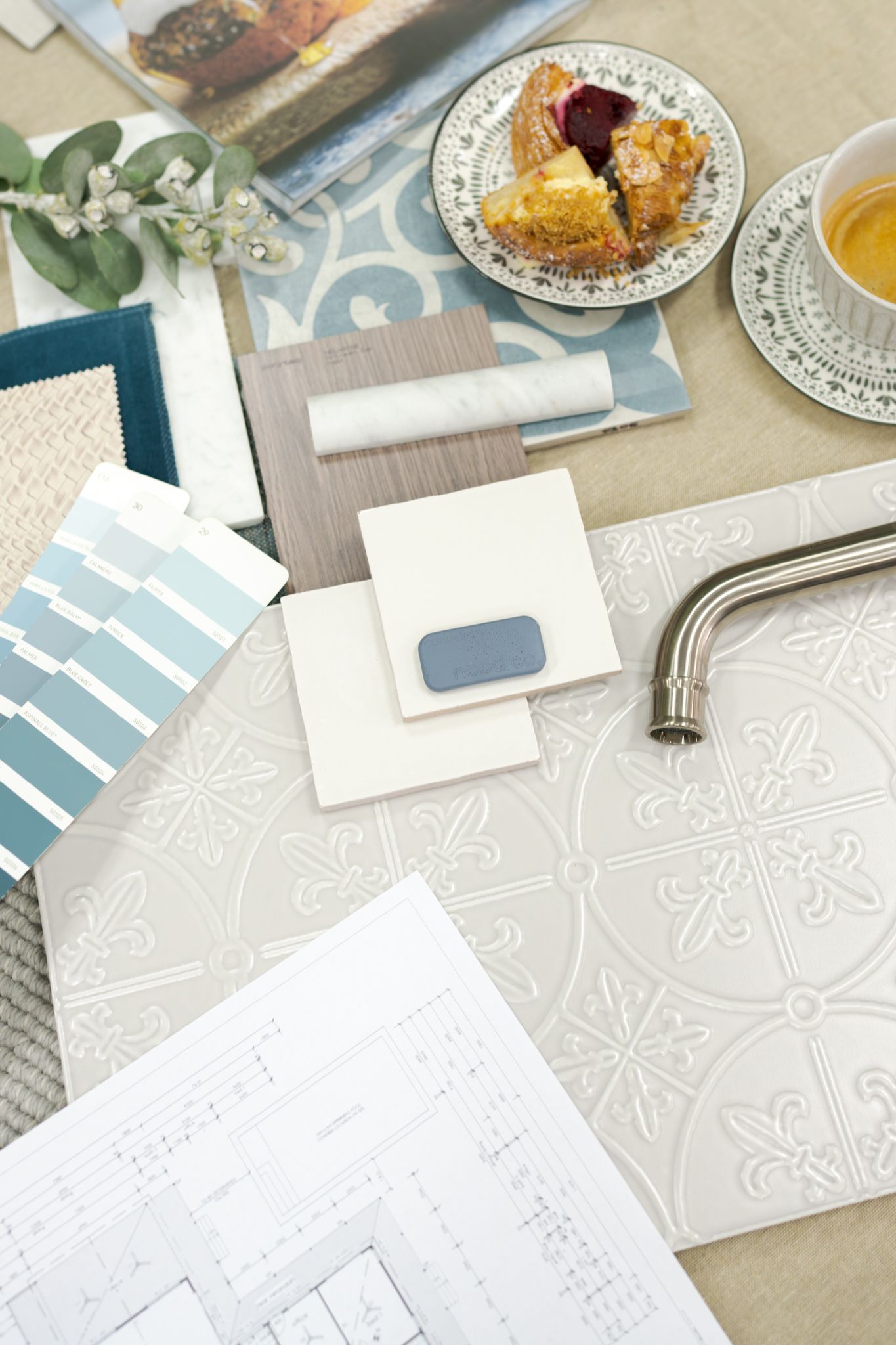 Flat lay of a desk with a patterned notebook, pen, iced drink, and small plate of fruit on a beige surface