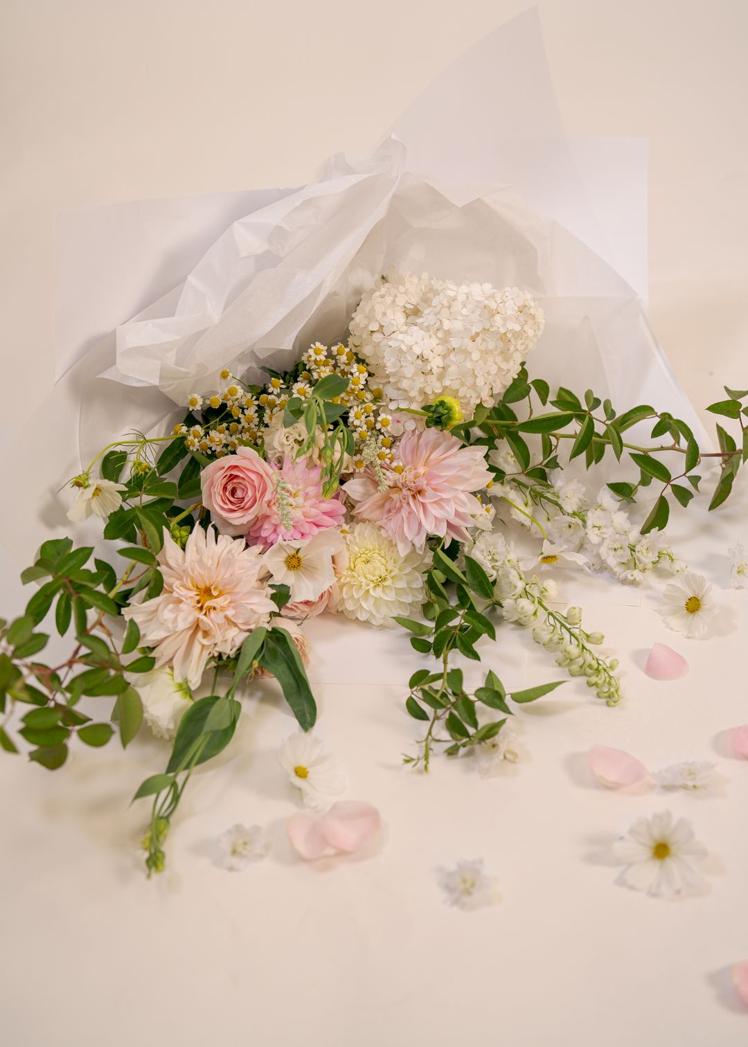 Loose bouquet of pink and white flowers with greenery, wrapped in white tissue, on a light floral tablecloth