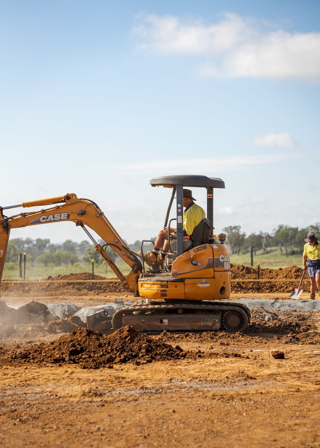 Yellow excavator working on a dusty construction site under a clear sky