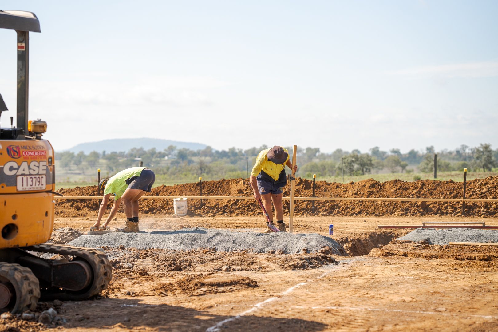 Construction workers pouring concrete at a roadwork site beside heavy machinery.