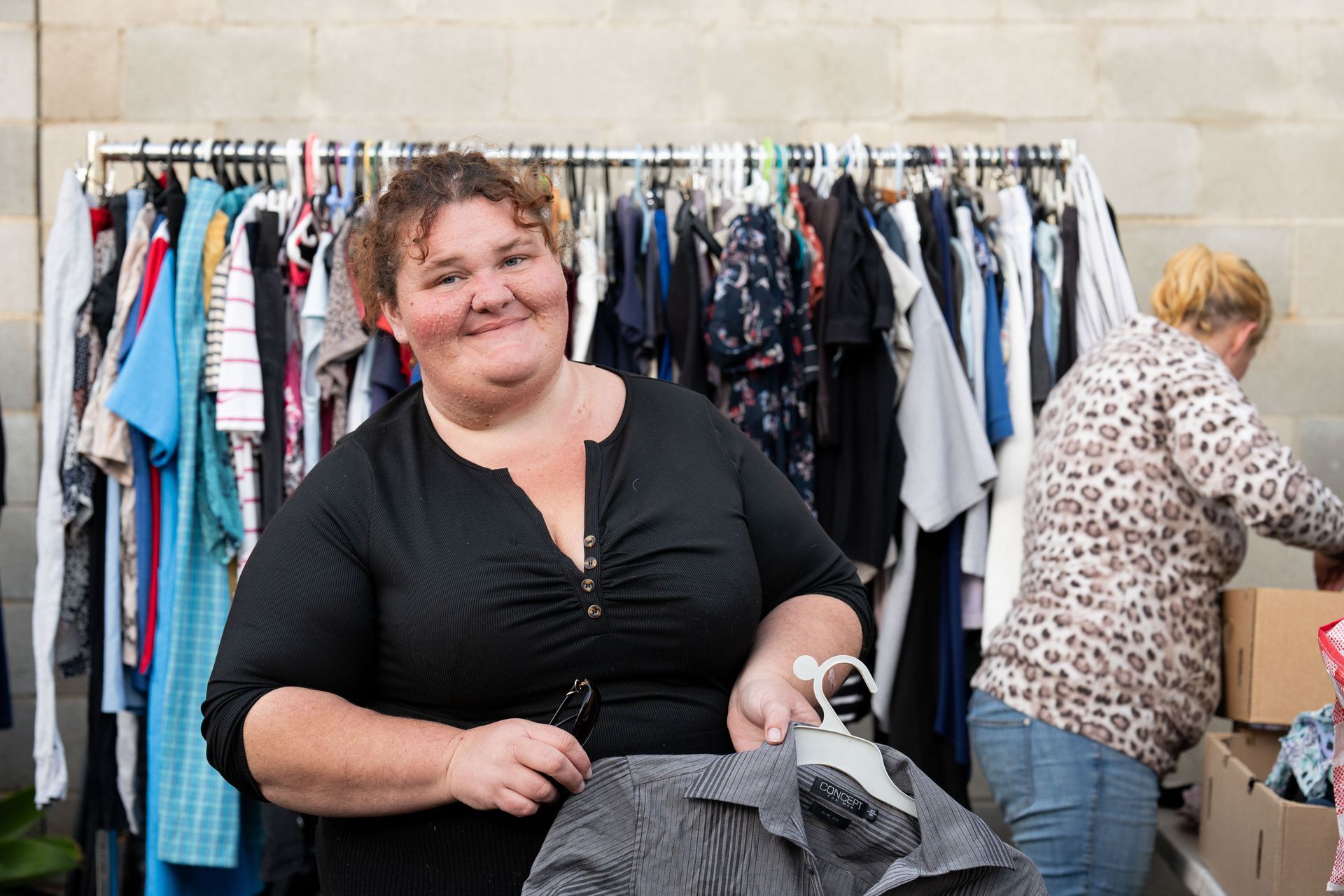 Woman smiling while holding clothes at a clothing swap with racks of garments in the background