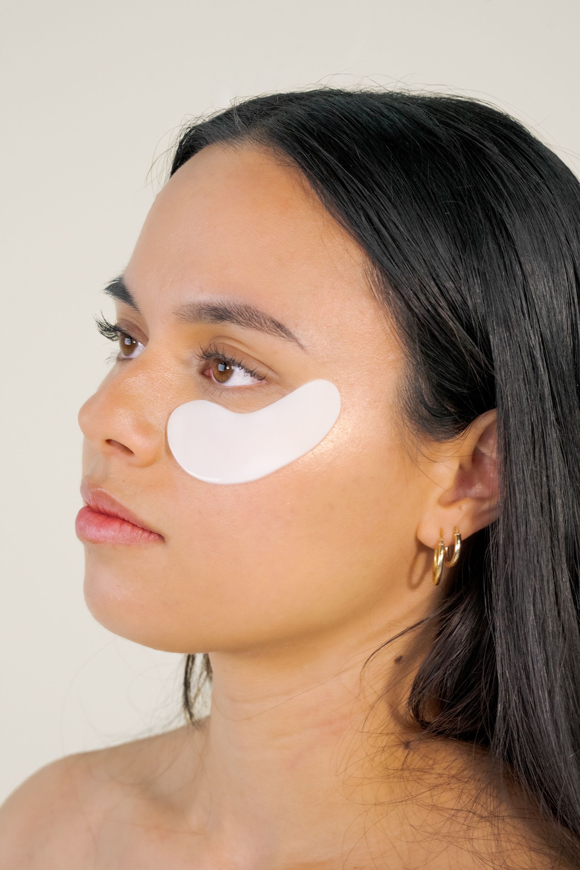 Woman wearing a white under-eye patch, shown in profile against a plain background