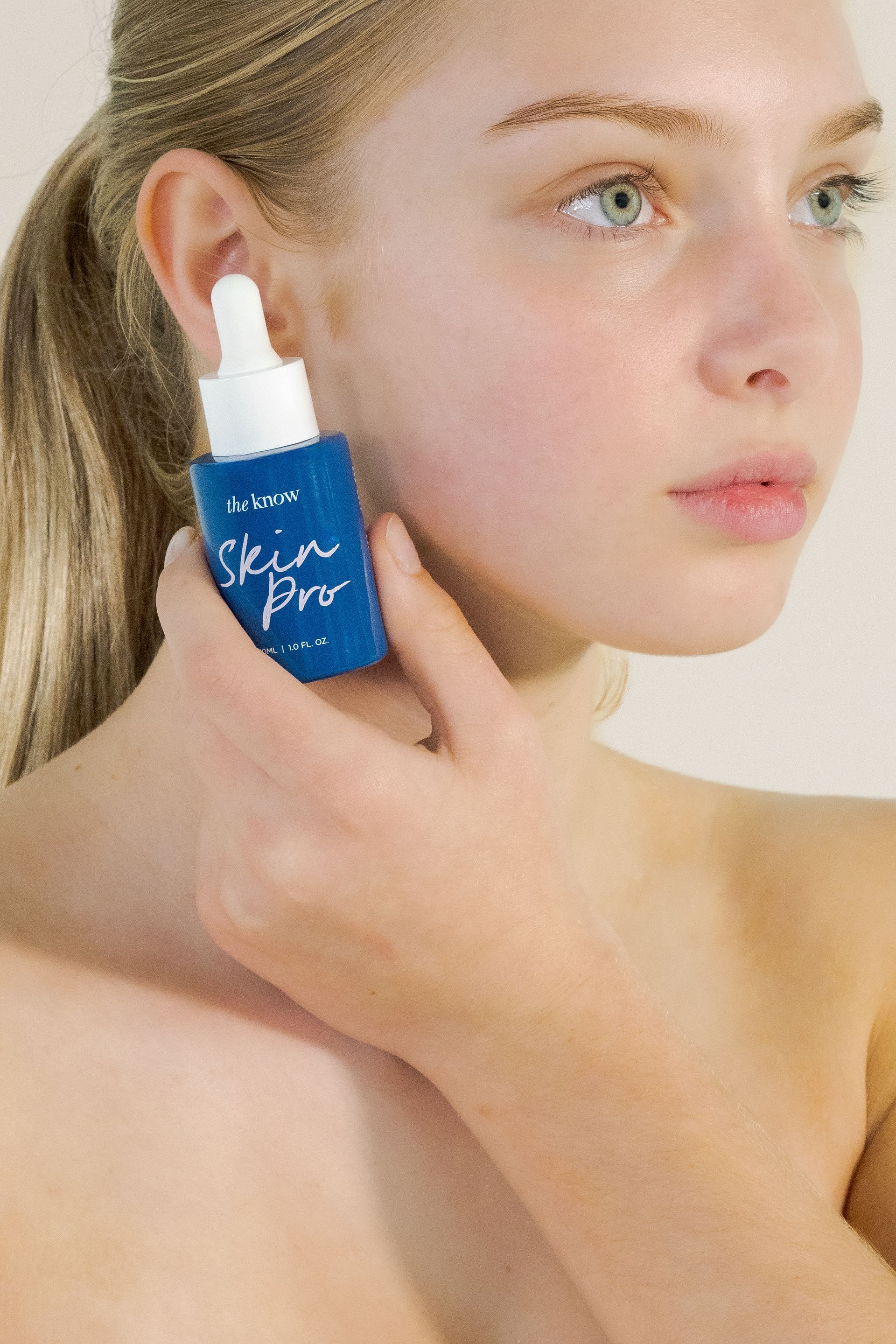 Woman applying blue dropper serum to her cheek, close-up skincare shot